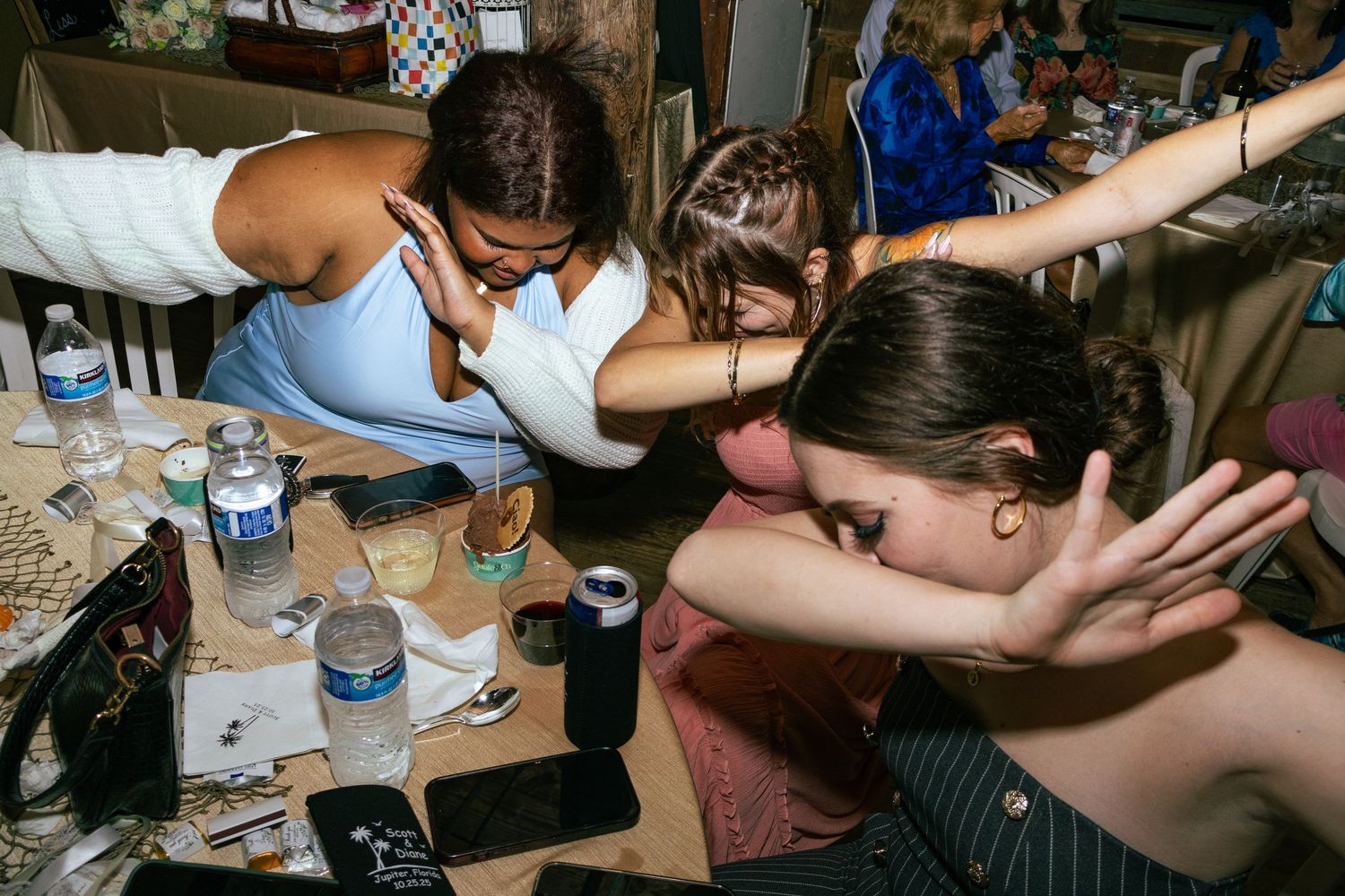 Group of young women laughing and leaning over a table at a party.