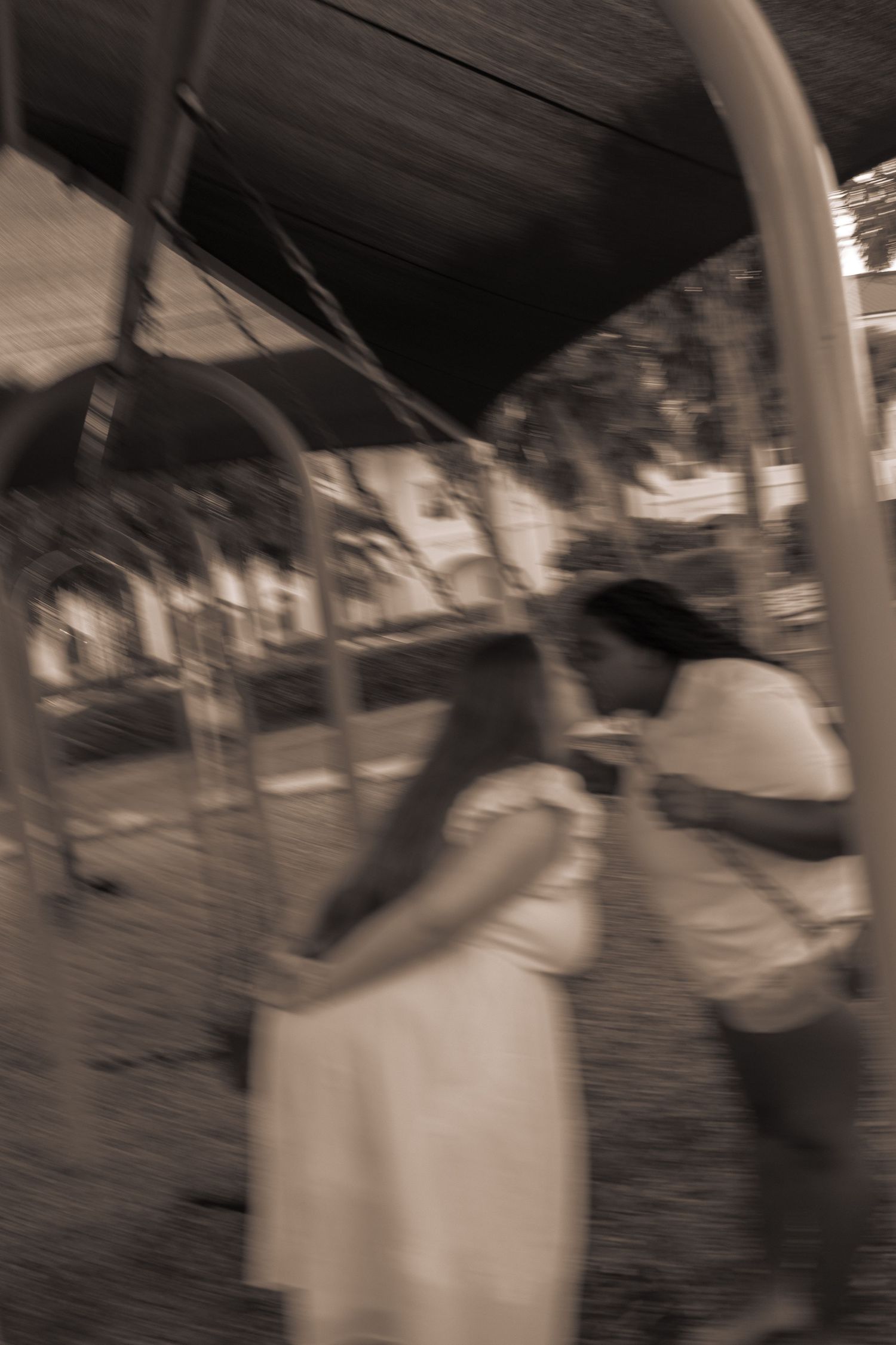 Blurry sepia photo of two women embracing near a playground swing set.