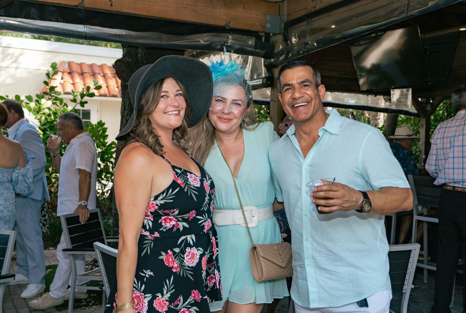 Three friends smile together at an outdoor Kentucky Derby themed celebration.