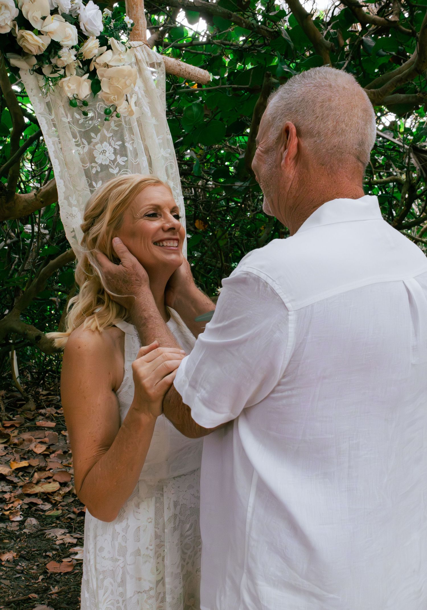 Groom tenderly cupping bride's face during emotional outdoor wedding ceremony.