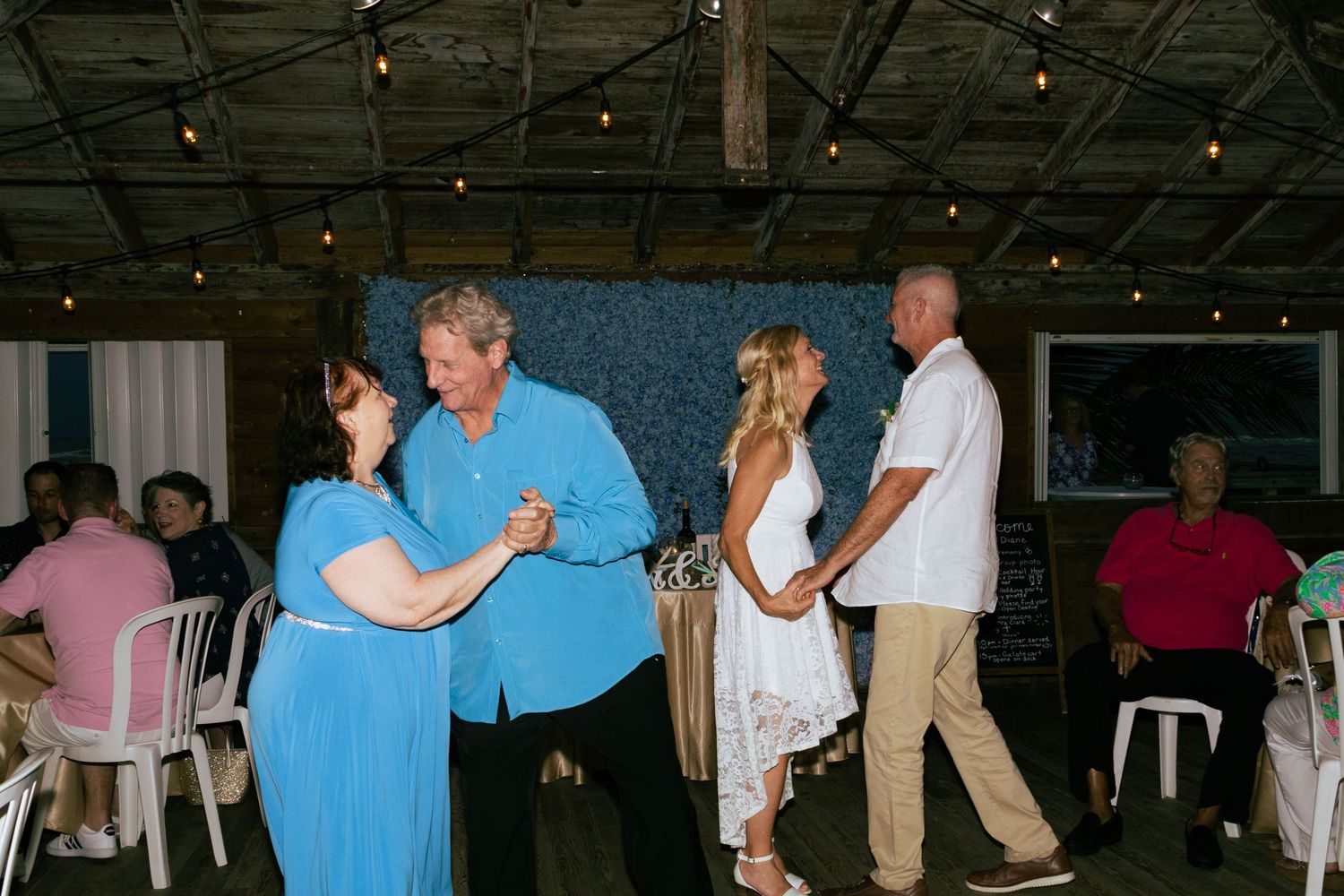 Couples dance together at casual tropical wedding reception with string lights.