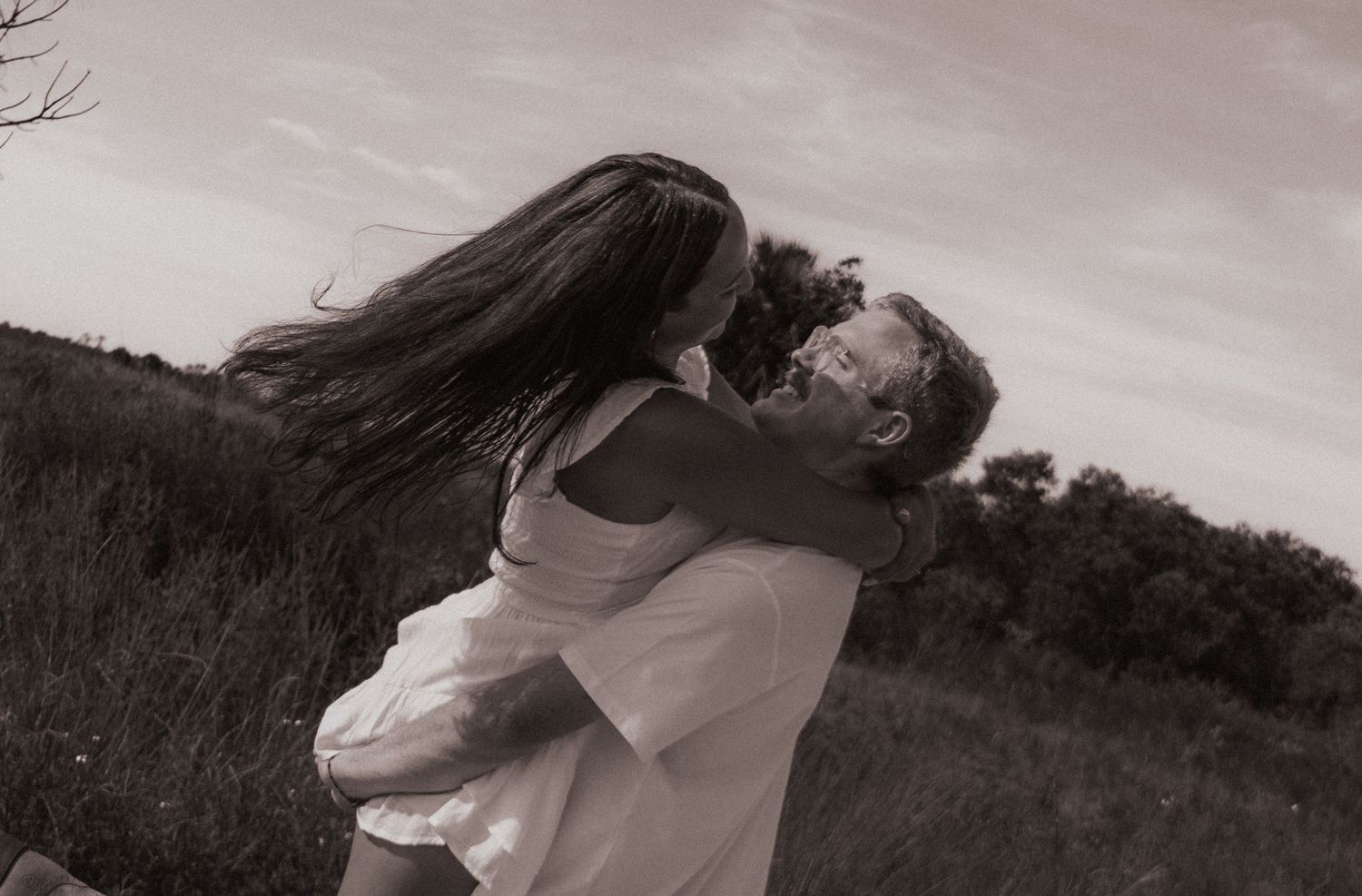 Black and white photo of a man lifting and embracing a woman in a field.