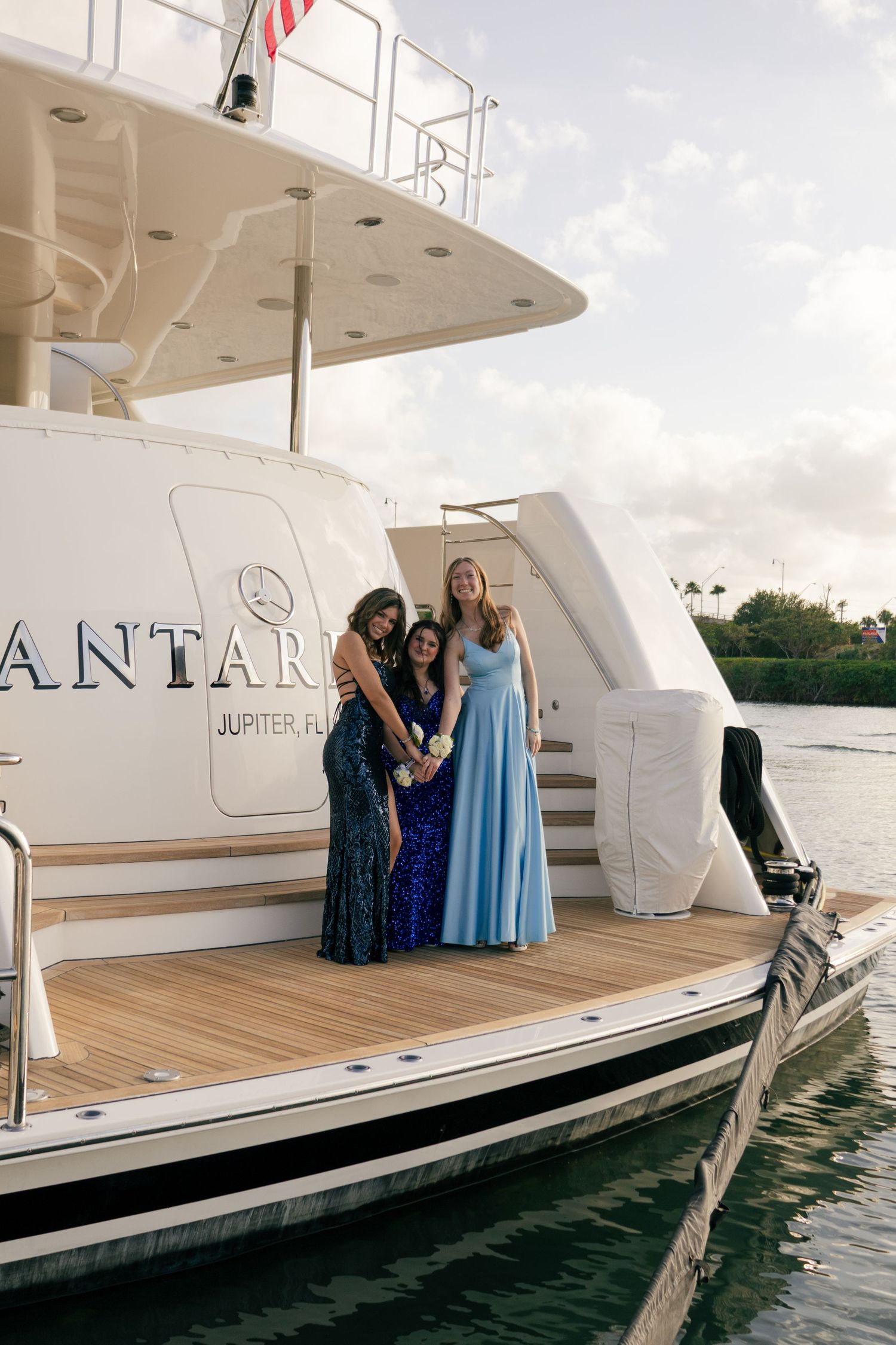 Three young women in formal gowns posing on the deck of a luxury yacht in Jupiter, Florida.