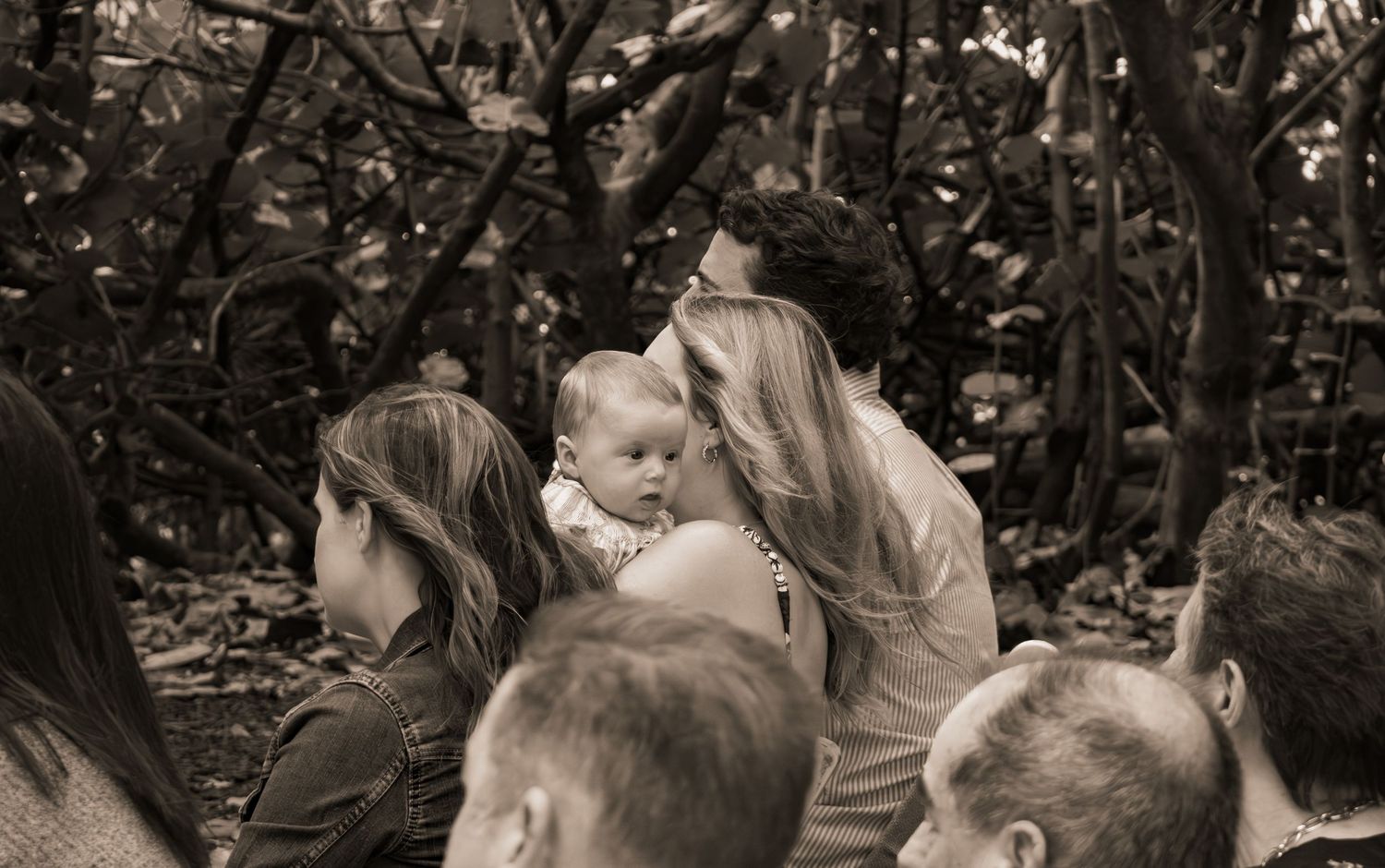 Wedding guests including mother with baby watch outdoor ceremony in black and white.