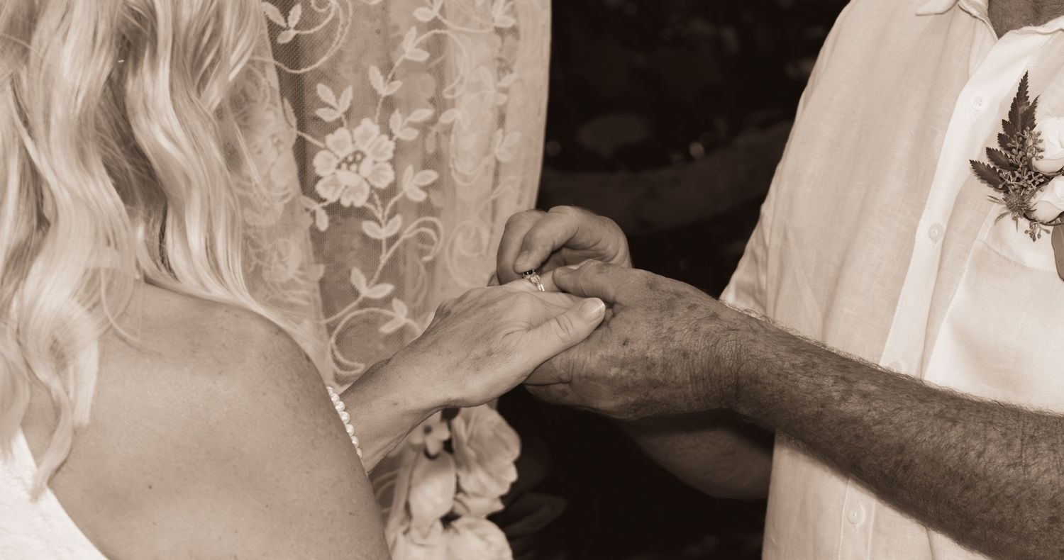 Sepia-toned close-up of a couple exchanging wedding rings during an outdoor marriage ceremony.