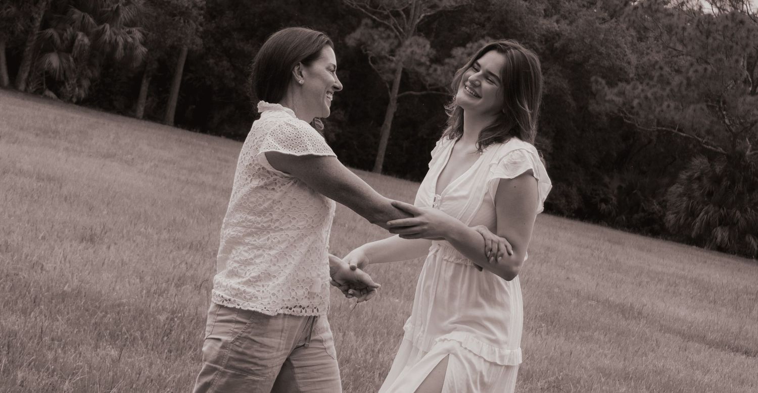 Black and white photo of two people holding hands and dancing together in a grassy outdoor field.