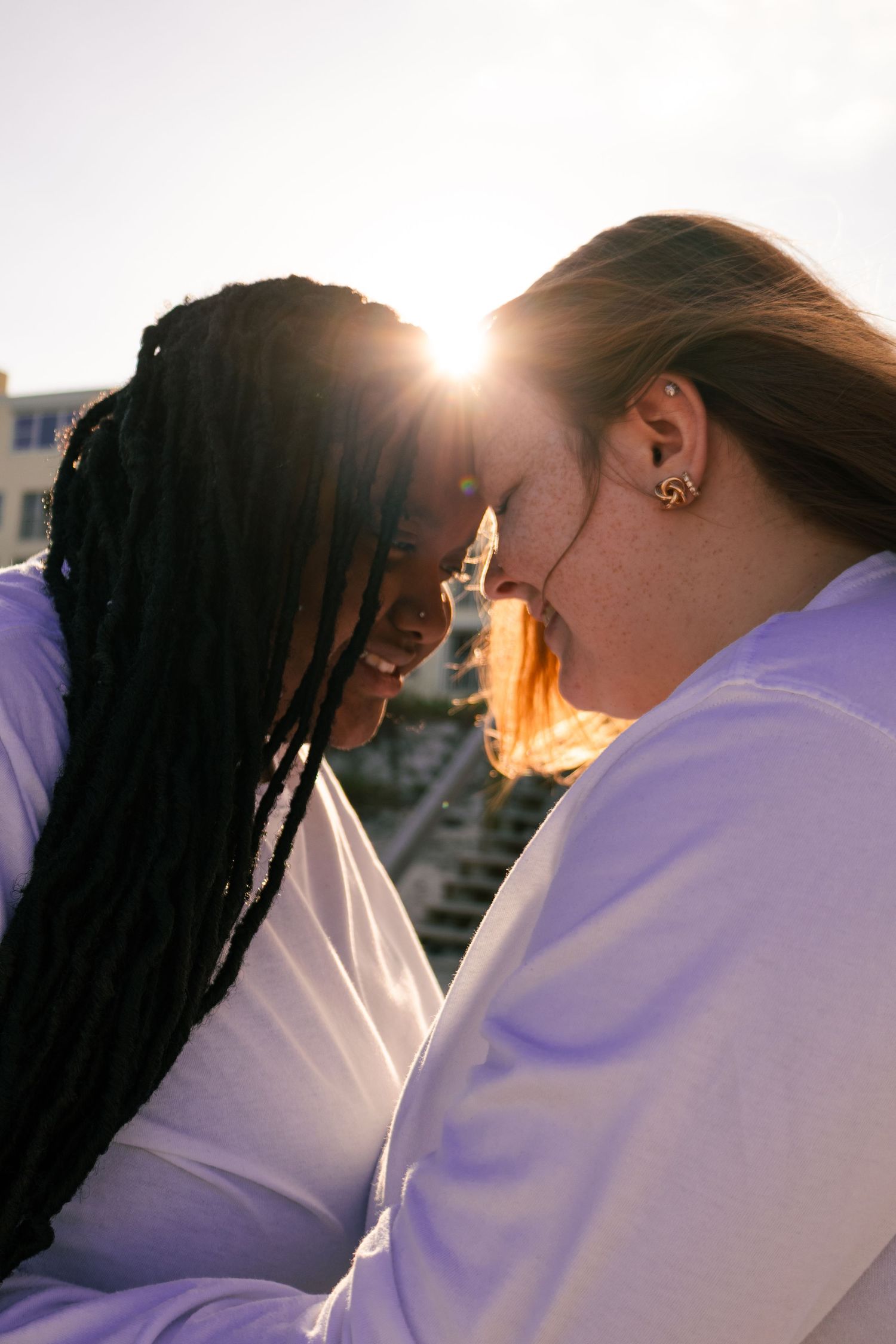 Two women touching foreheads with sunlight glowing between them outdoors.