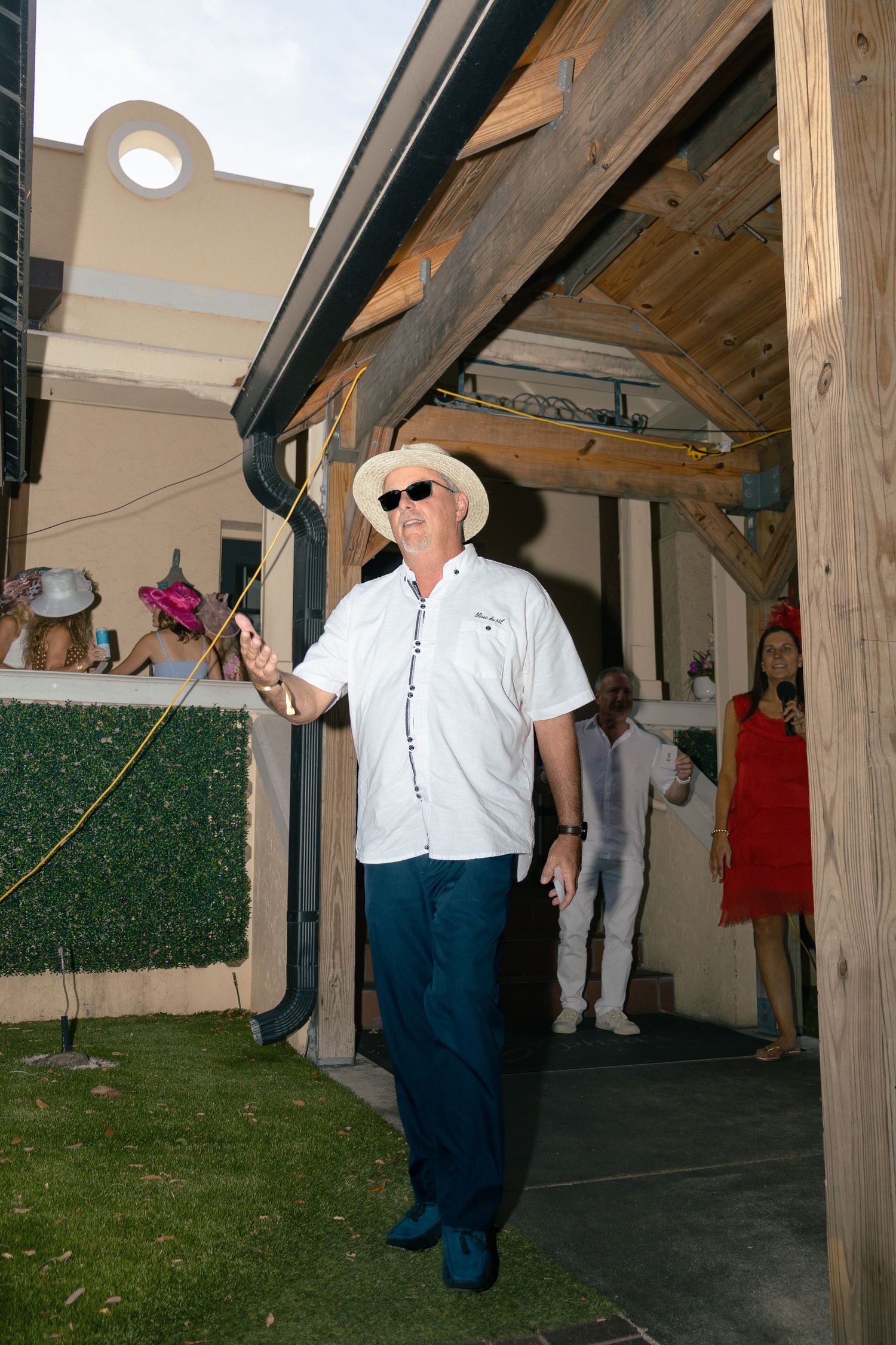Man in white shirt and panama hat walks through outdoor venue at Kentucky Derby party.