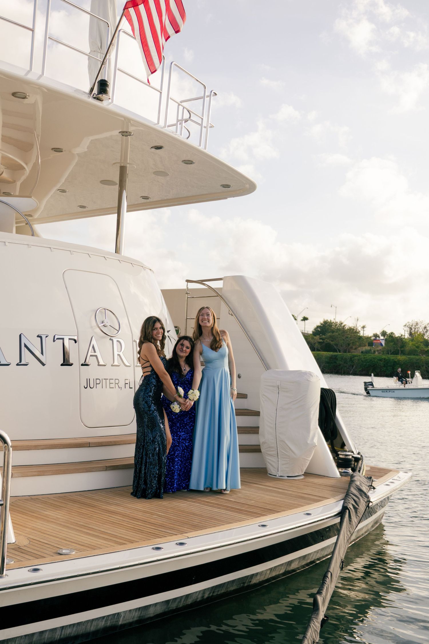 Three teenage girls in sequin and satin prom dresses pose on the deck of a luxury yacht in Jupiter, Florida.