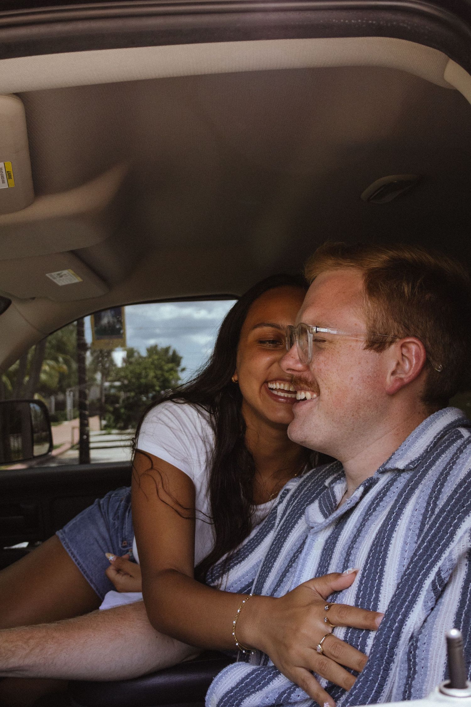 Happy interracial couple laughing together while sitting inside a car on a sunny day.