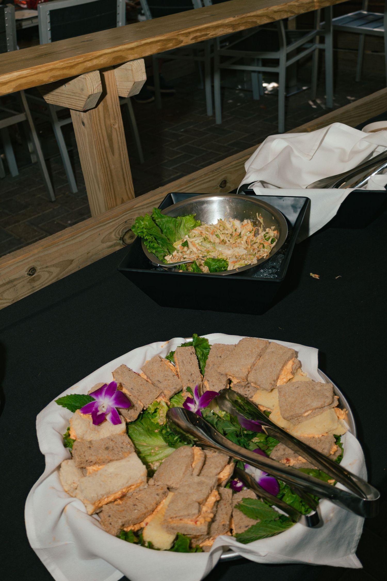Elegant buffet table with sliced meatloaf garnished with purple orchids and a bowl of noodle salad on a black tablecloth.
