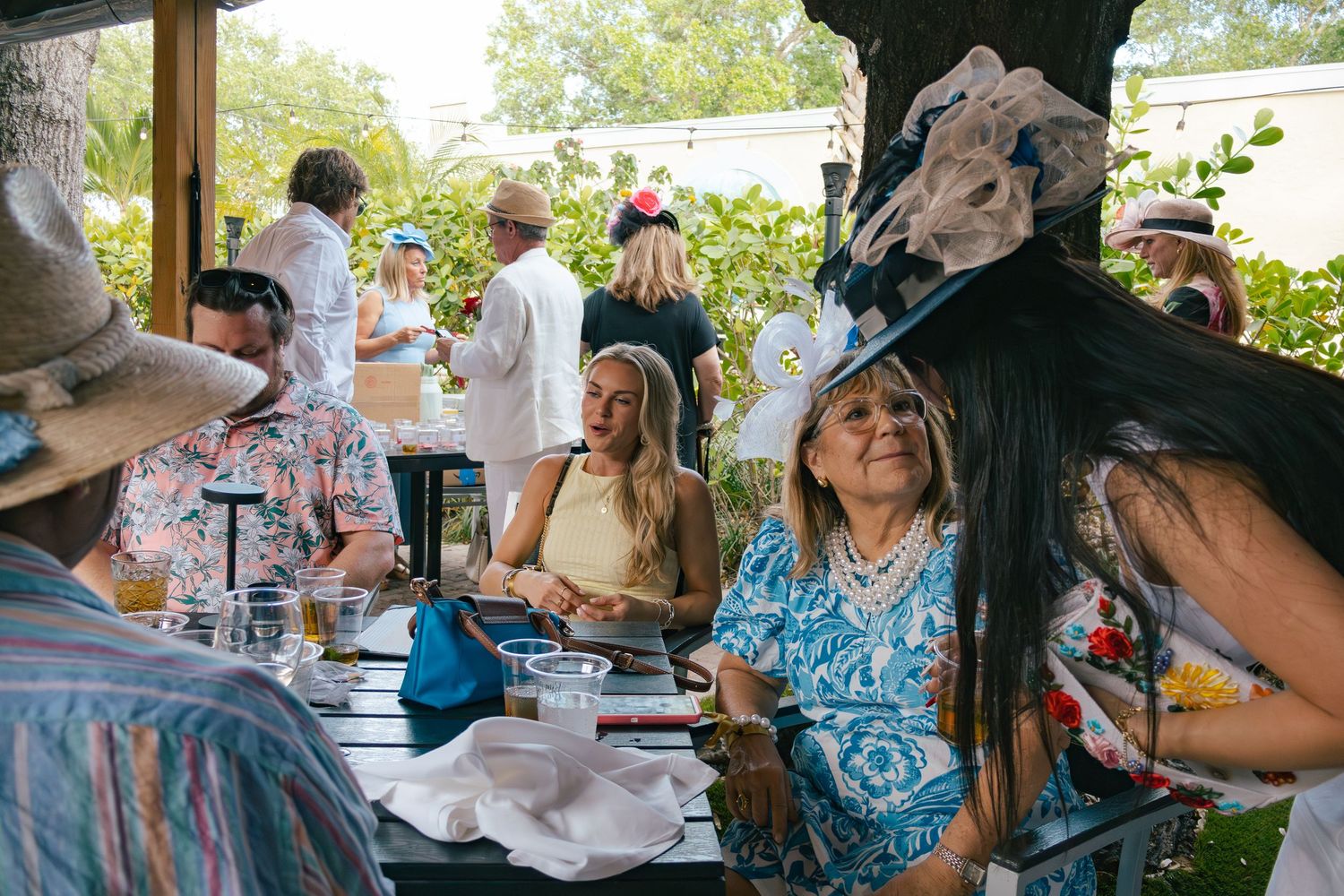 Guests in decorative hats socialize at an outdoor Kentucky Derby themed garden party.
