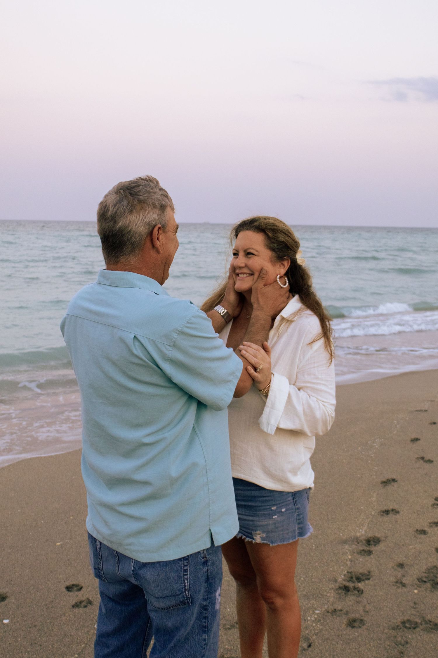 Smiling middle-aged couple sharing a romantic moment on a sandy beach at sunset.
