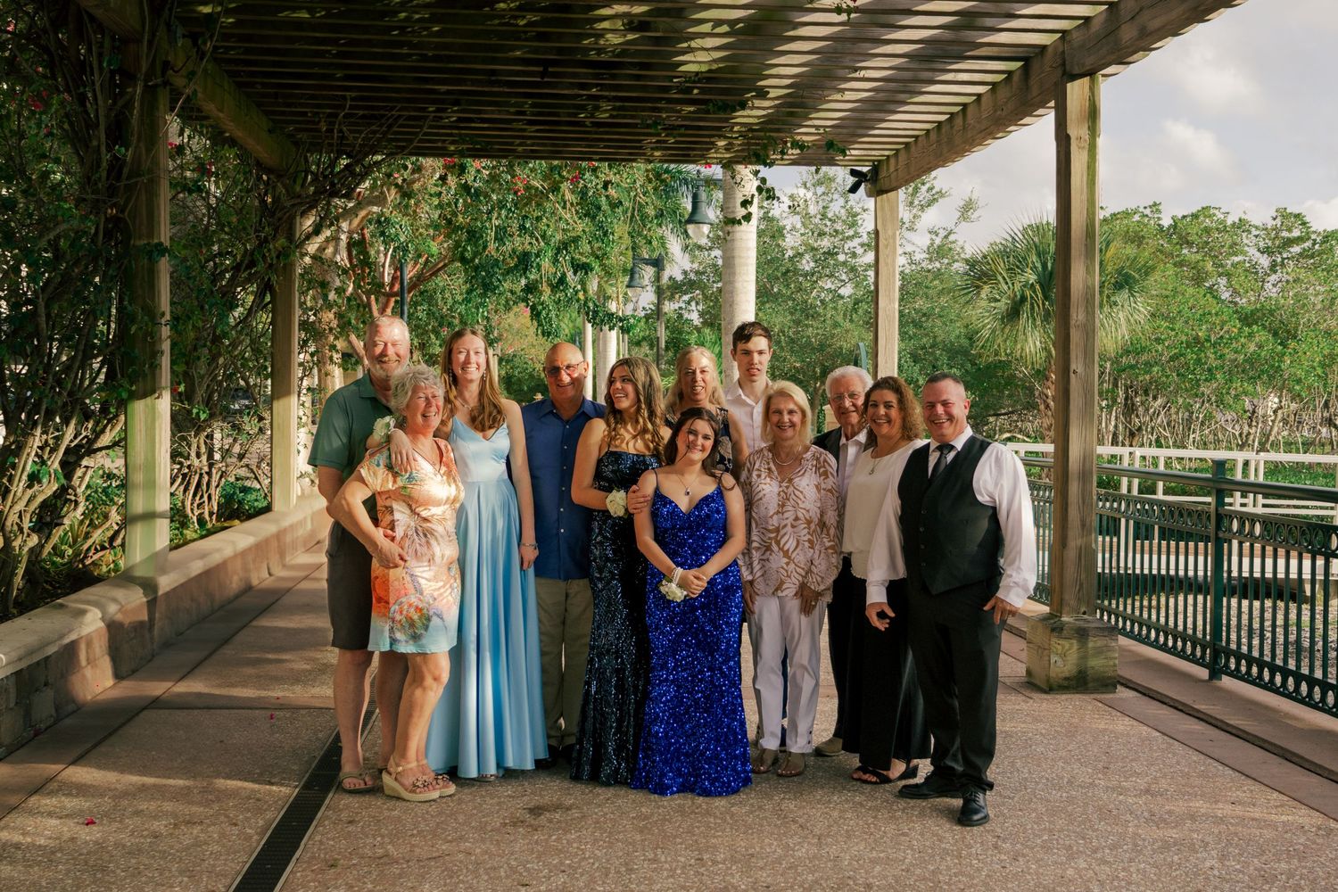 Large family group in formal attire posing together under outdoor pavilion for prom photos.