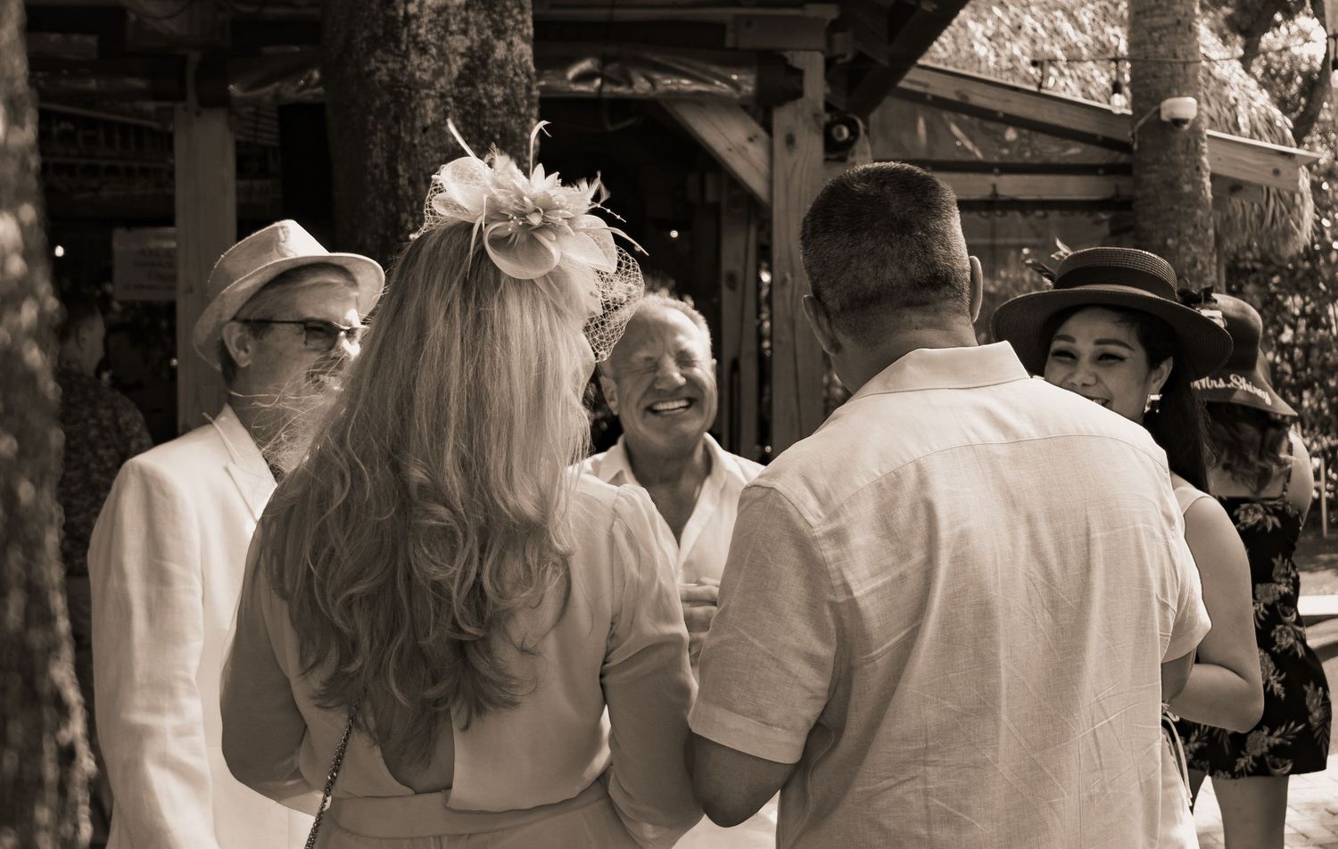 Sepia-toned photo of elegantly dressed guests socializing outdoors at a garden wedding celebration.