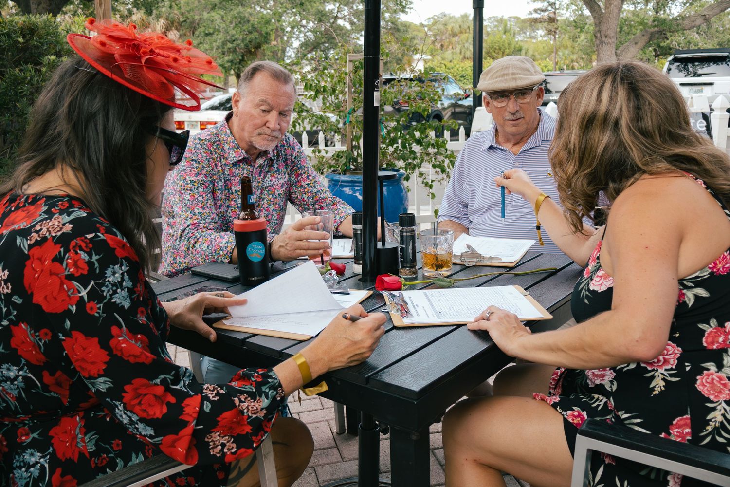 Four people reviewing menus at outdoor restaurant table wearing festive Kentucky Derby attire.