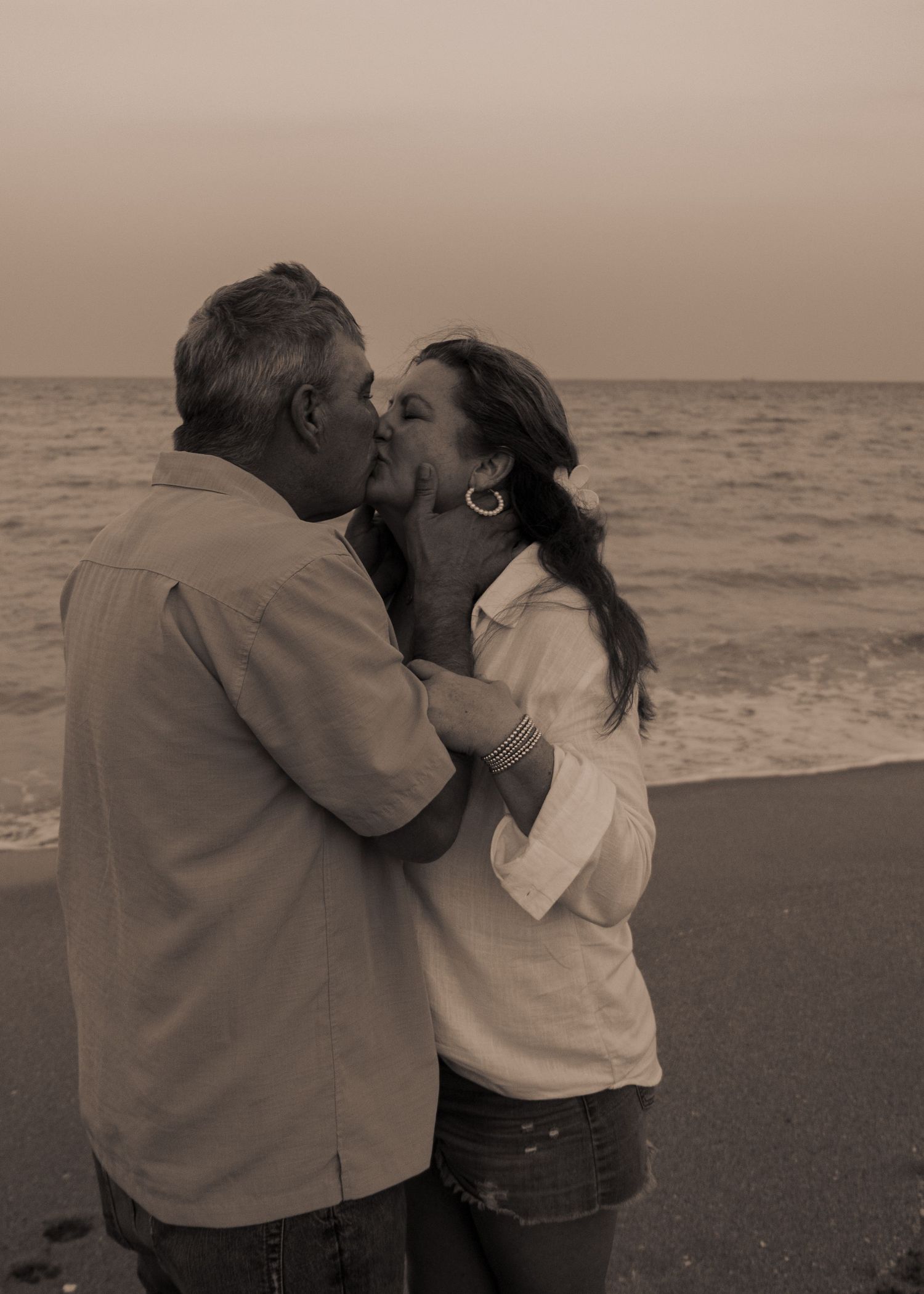 Couple sharing romantic kiss on beach at sunset in warm-toned sepia photograph.