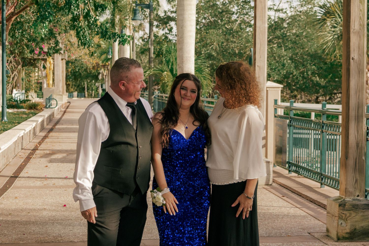 Three people smiling together outdoors near decorative columns, dressed in formal event attire.