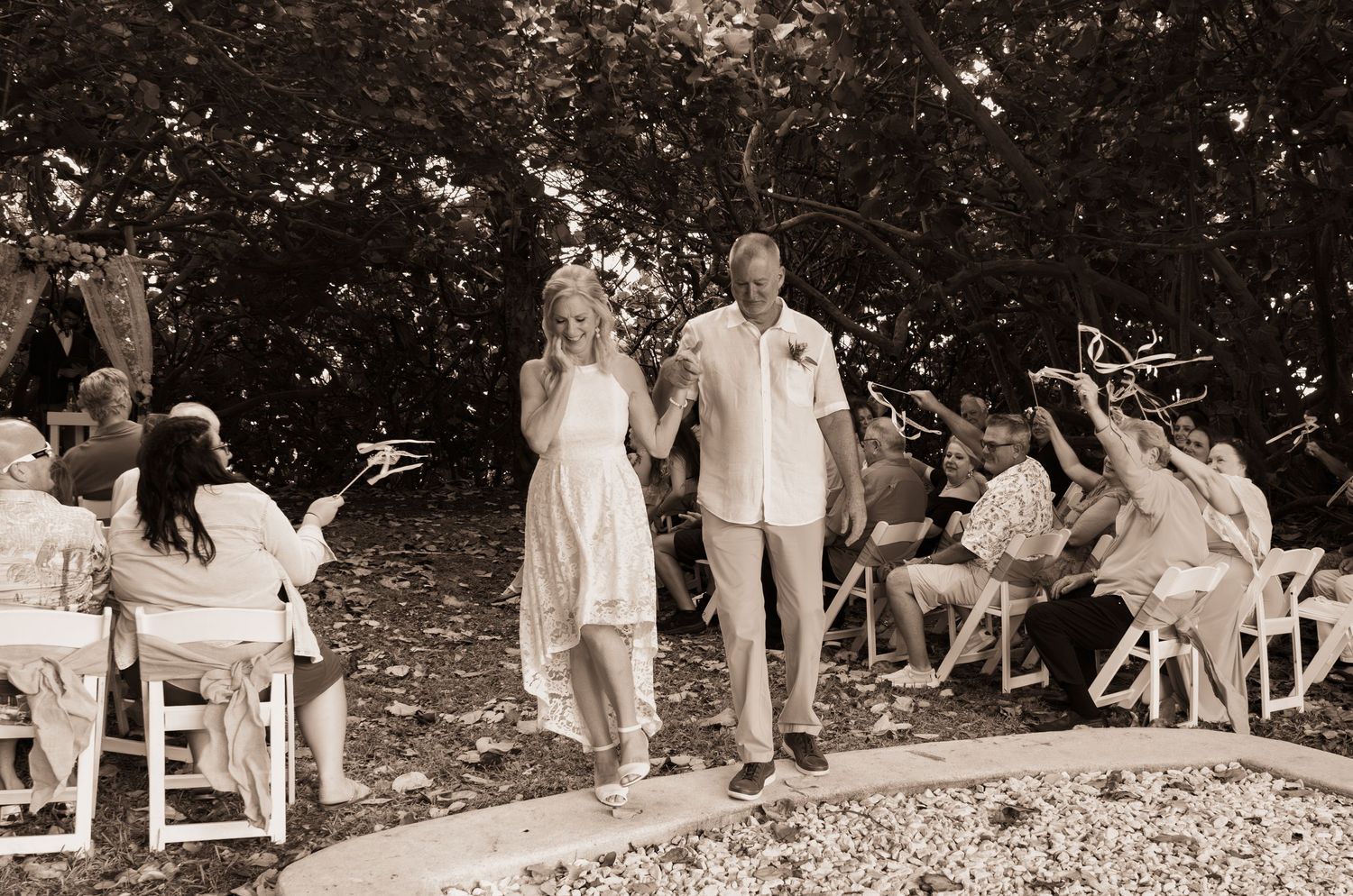 Black and white photo of newlyweds walking down aisle as guests celebrate with sparklers.