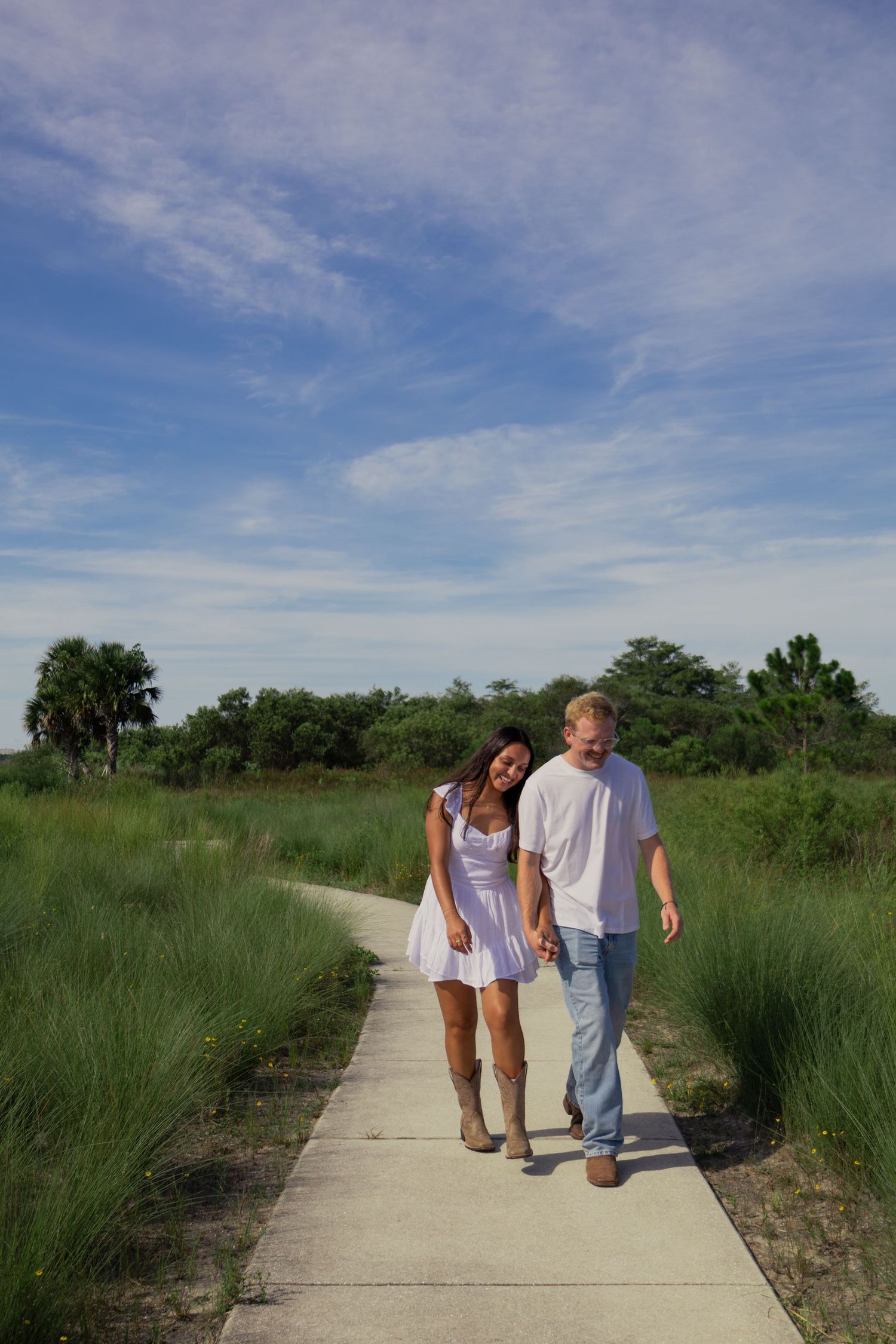 Couple walking hand in hand along a scenic pathway surrounded by lush green meadows.