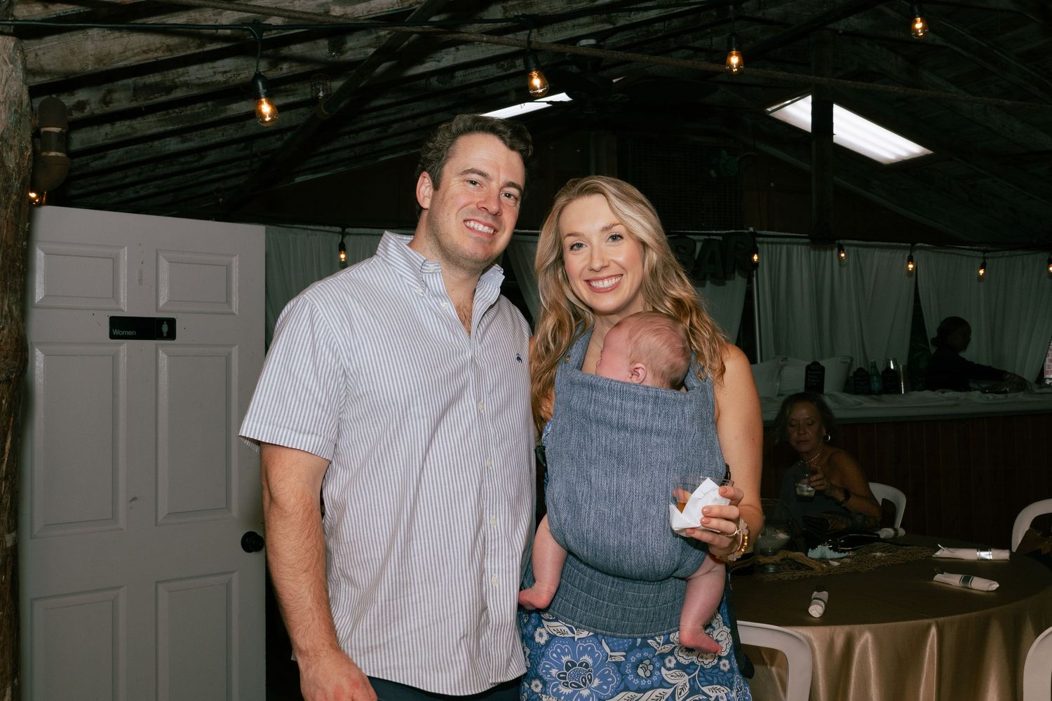 Smiling couple poses with newborn baby at wedding reception venue.