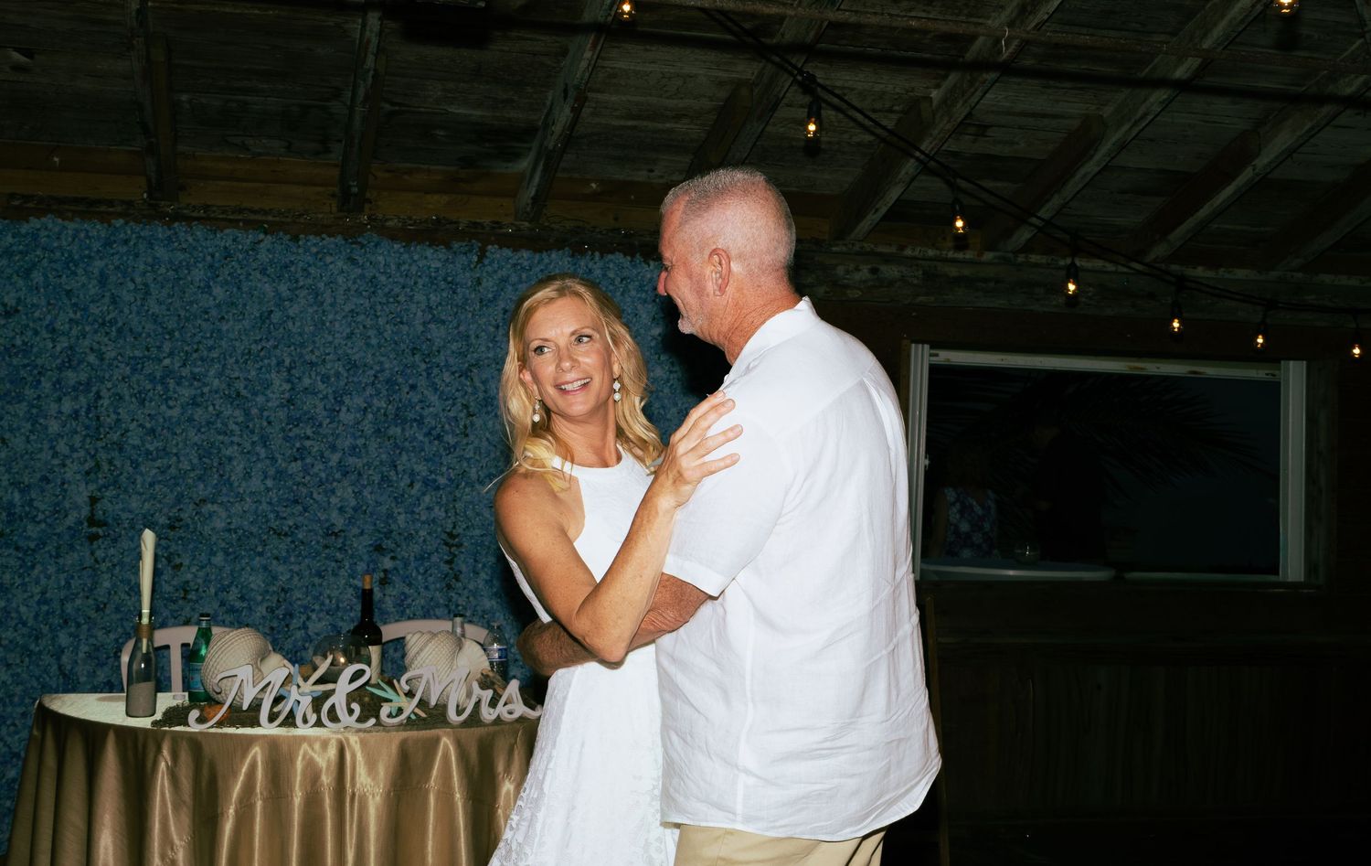 Bride and groom share their first dance at wedding reception with Mr and Mrs sign in background.