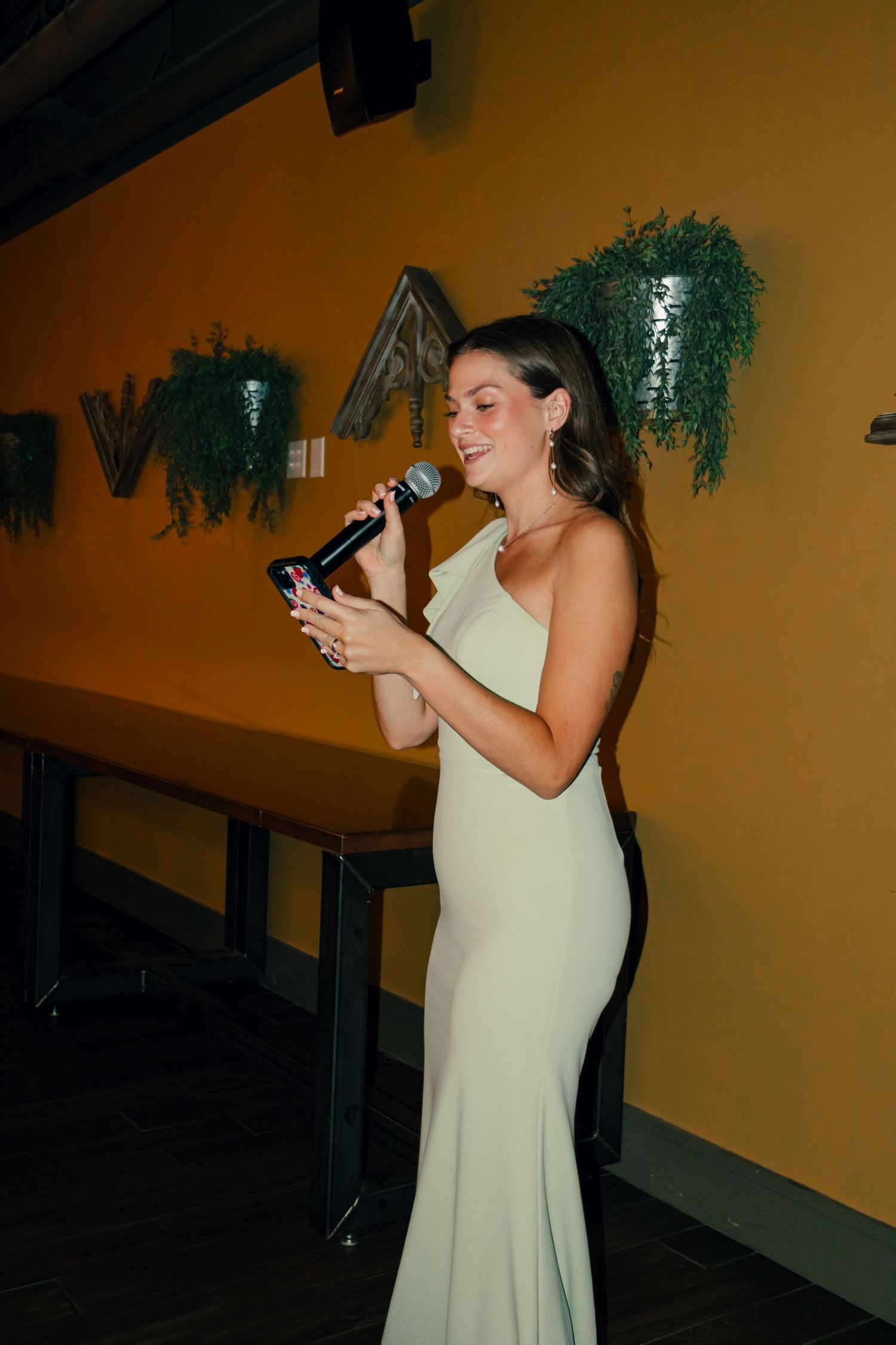 Elegant woman in sage green gown giving a speech with microphone at event.