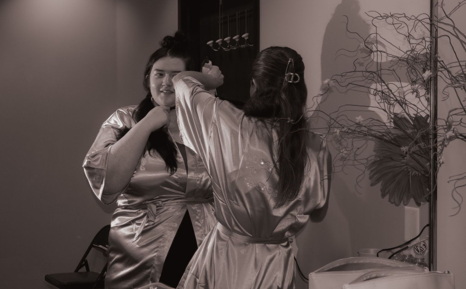 Black and white photo of bridesmaids helping each other with jewelry in robes.