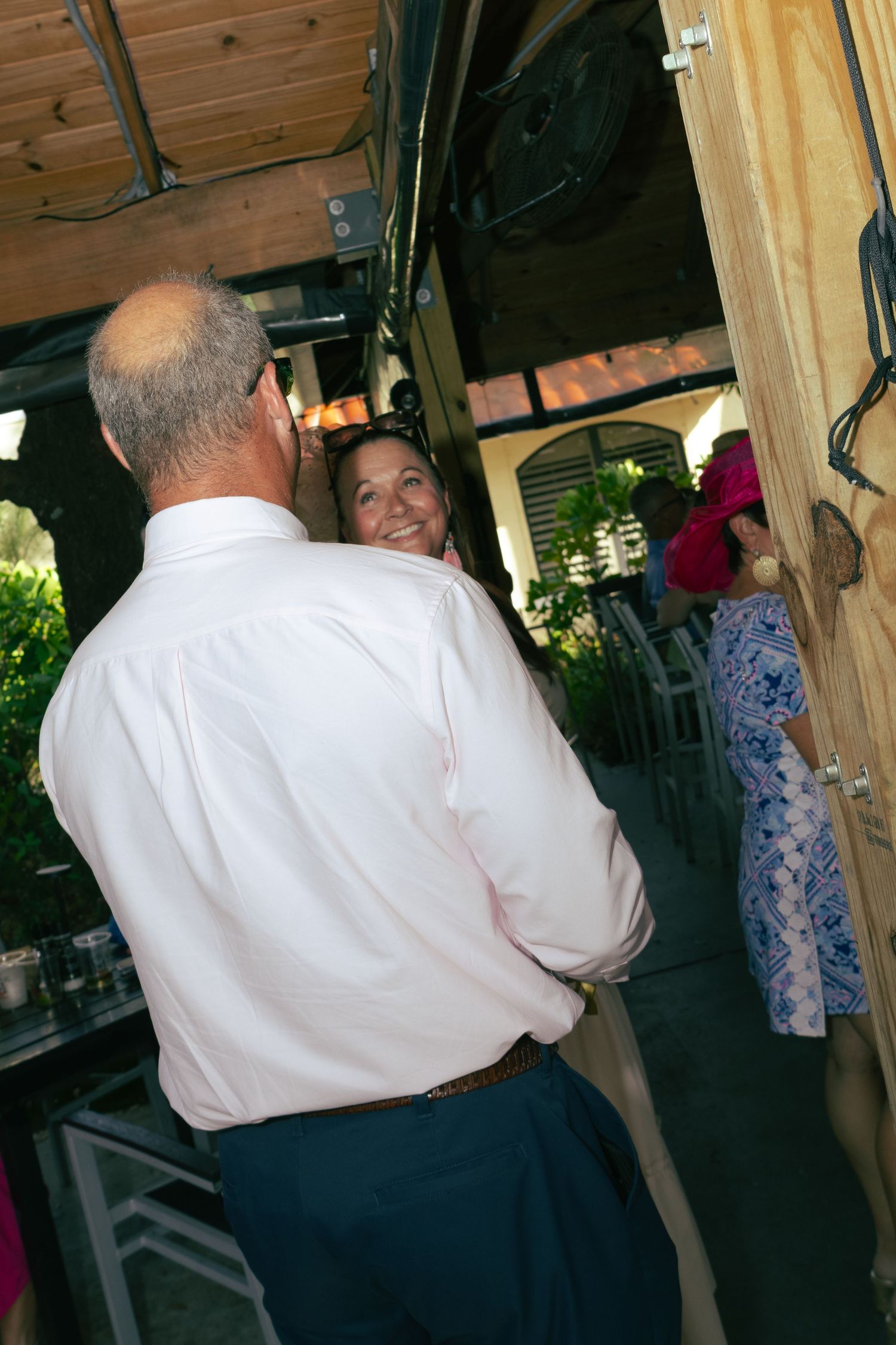 Man in pink dress shirt shares a smile with woman at an outdoor venue during a social gathering.