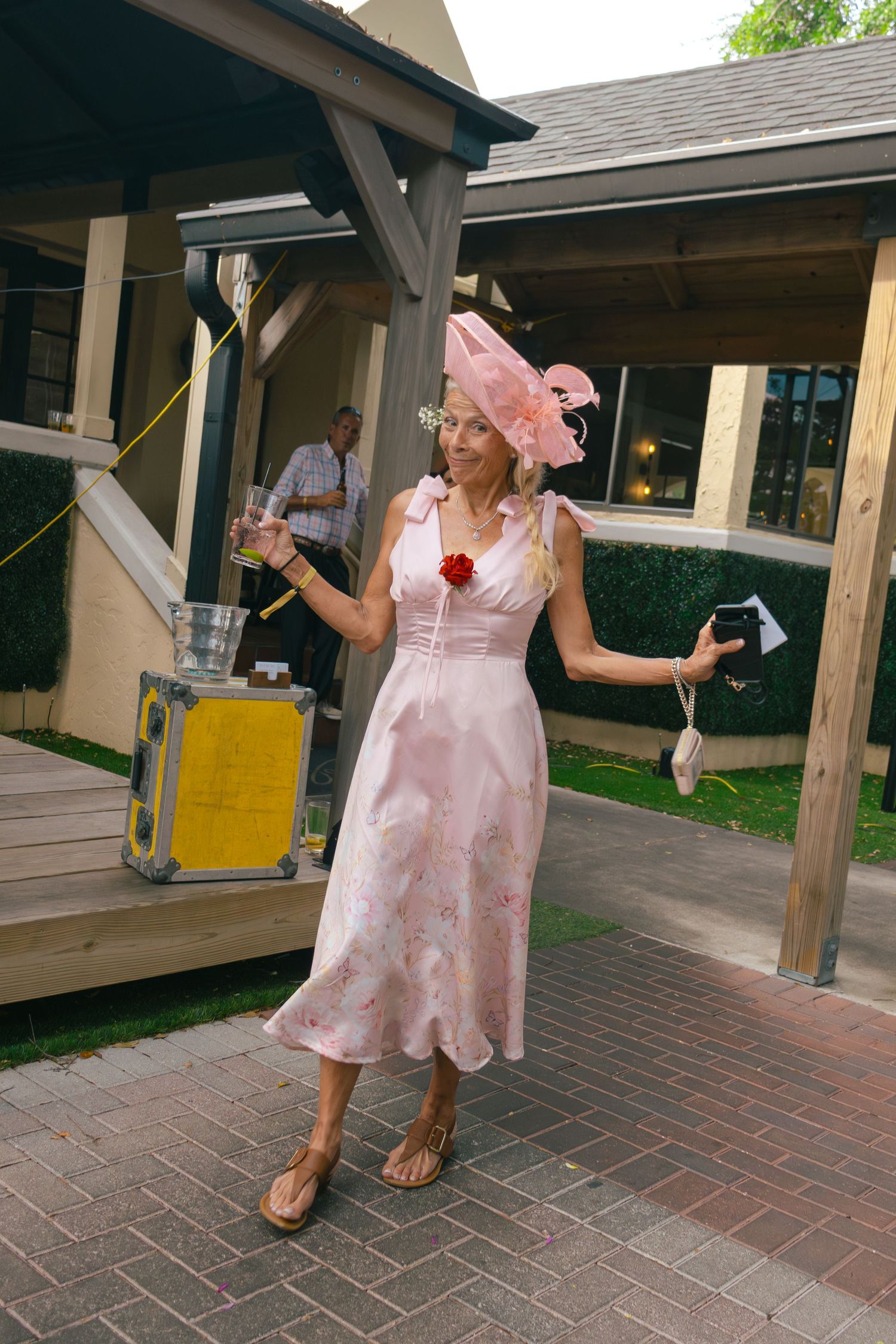 Woman in pink floral dress and pink fascinator poses at outdoor Kentucky Derby themed event.