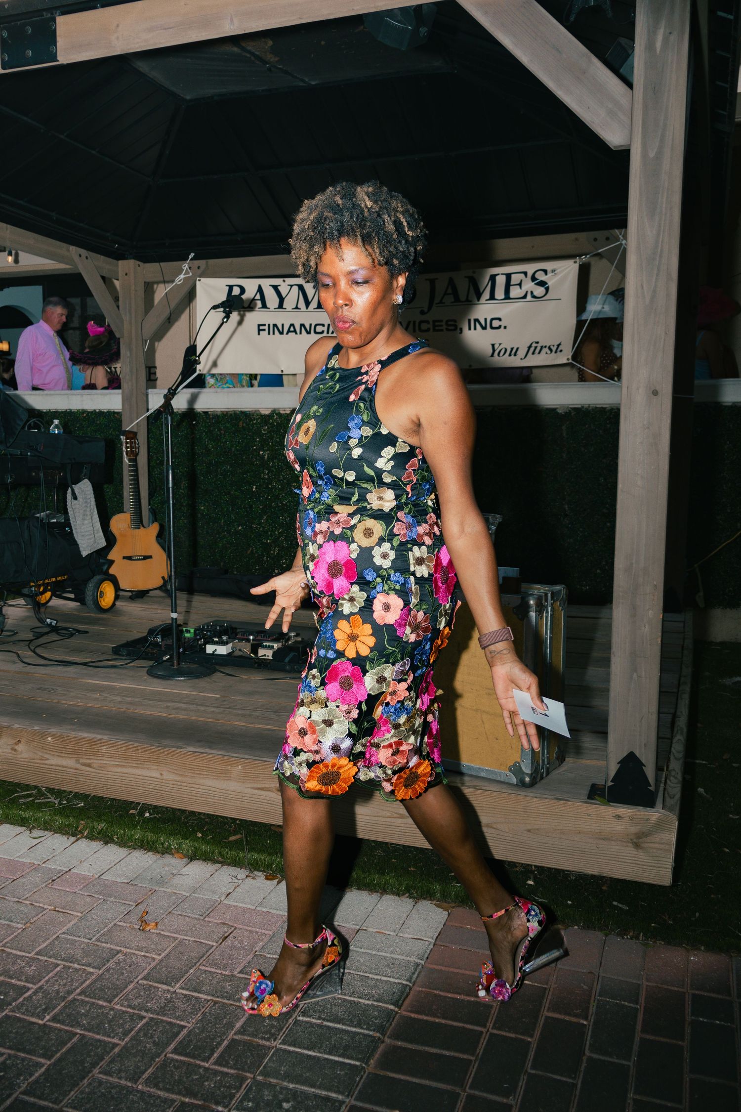 Woman in floral dress dancing at outdoor Raymond James financial event on brick patio.