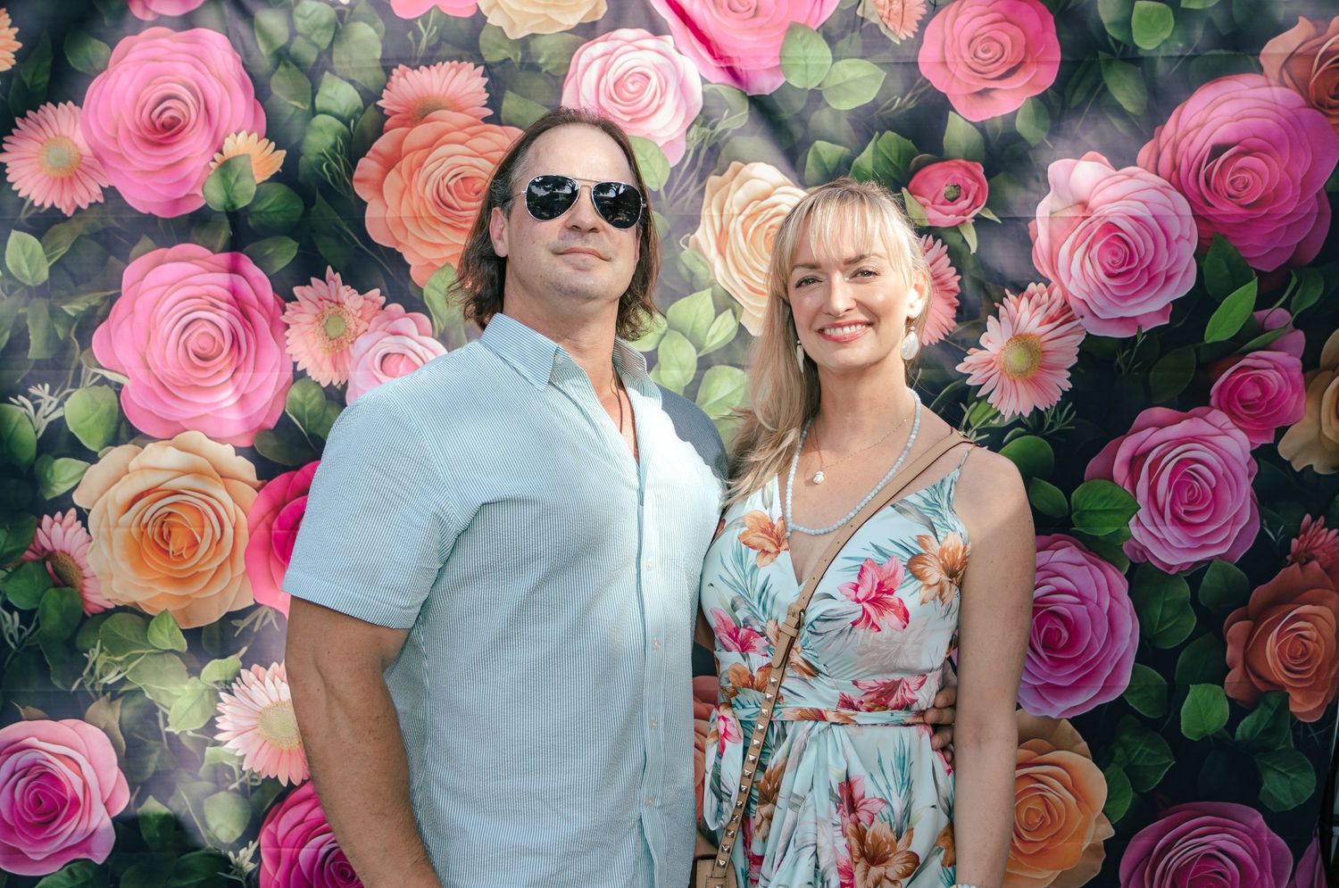 Couple posing together in front of a bright floral backdrop at a Kentucky Derby themed event.