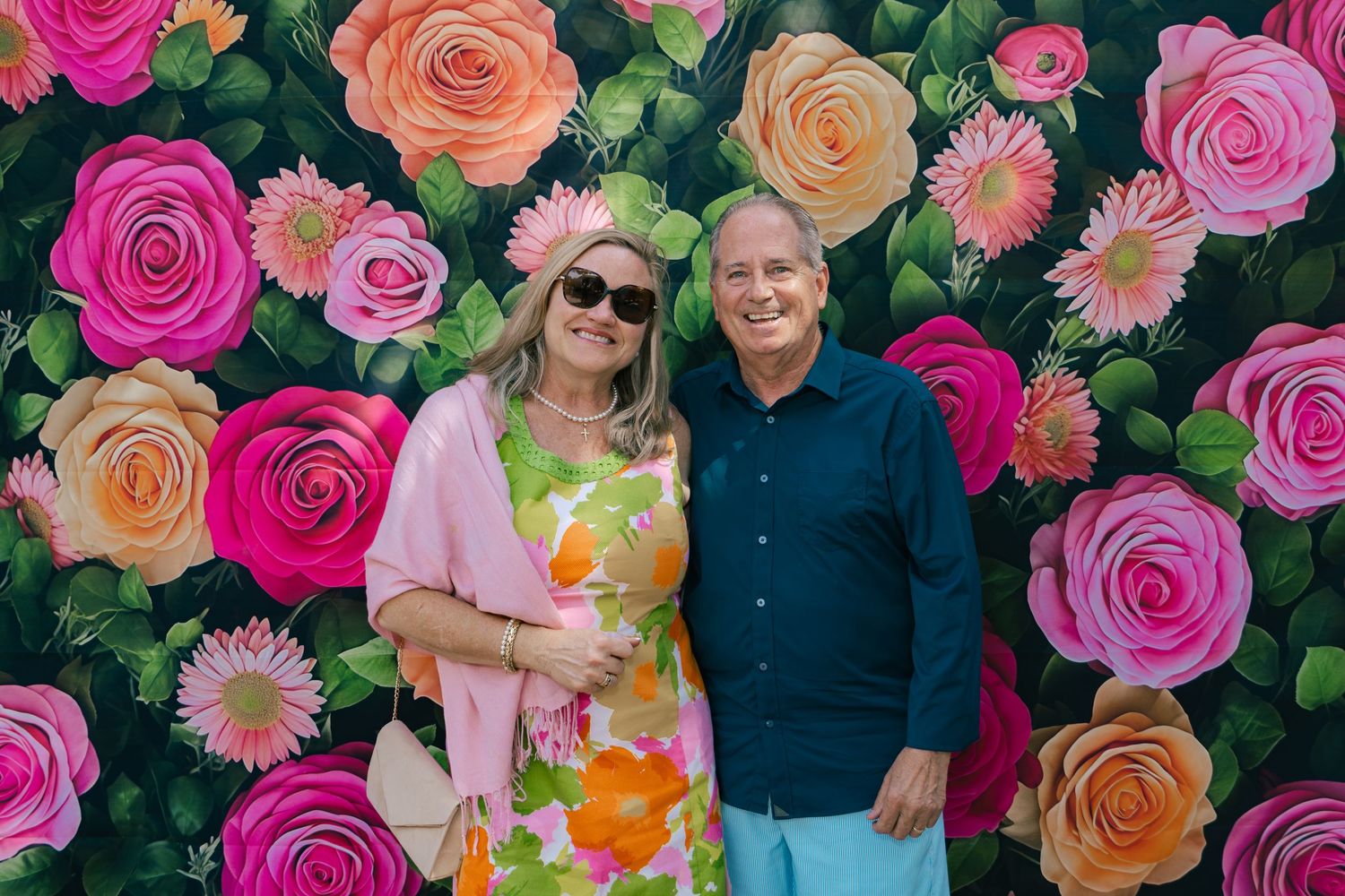 Couple posing in front of colorful floral rose backdrop at Kentucky Derby party.