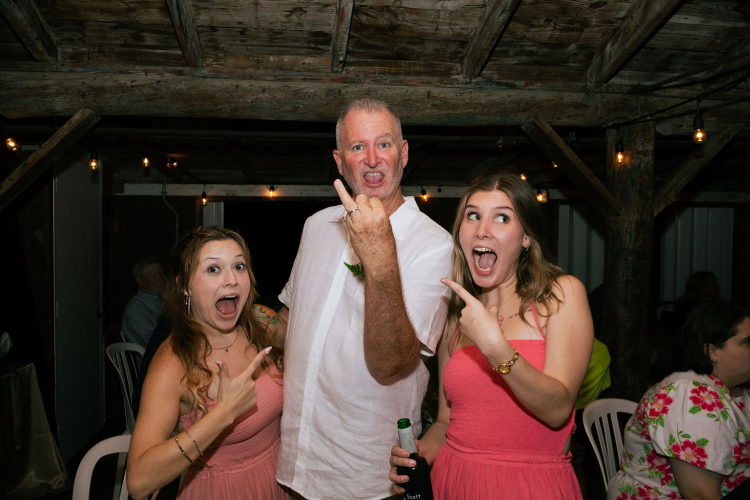 Man with two women making rock signs and excited faces at wedding party.