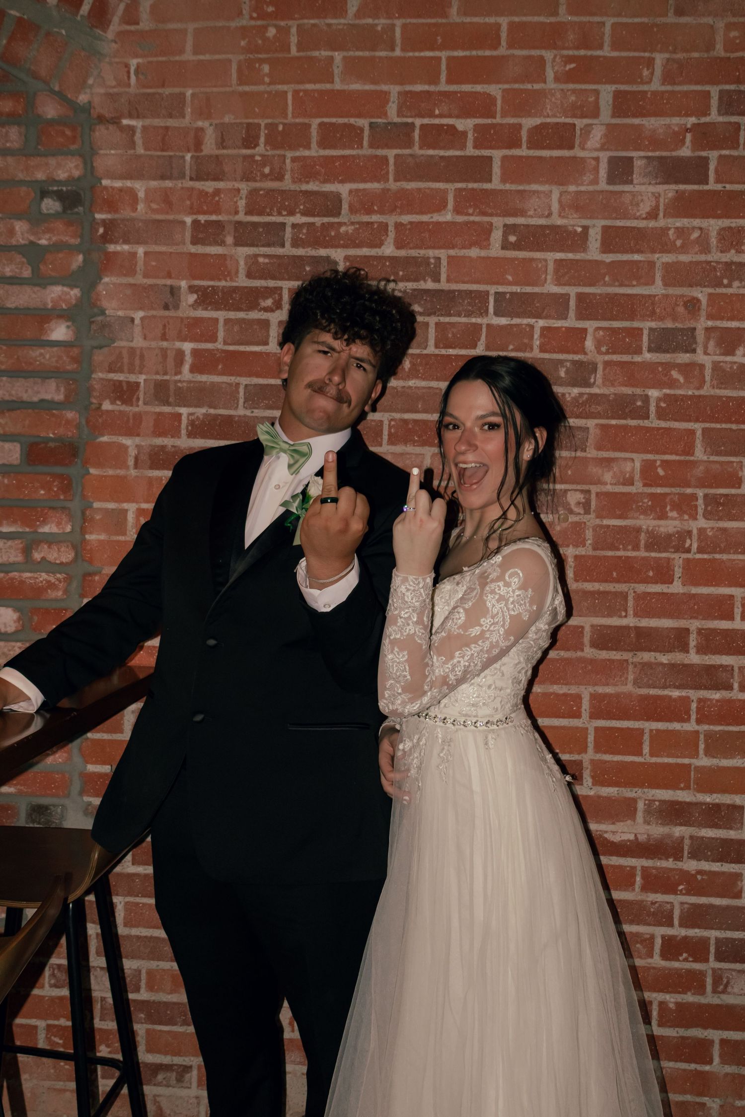 Happy newlyweds showing wedding rings at brick wall reception venue.