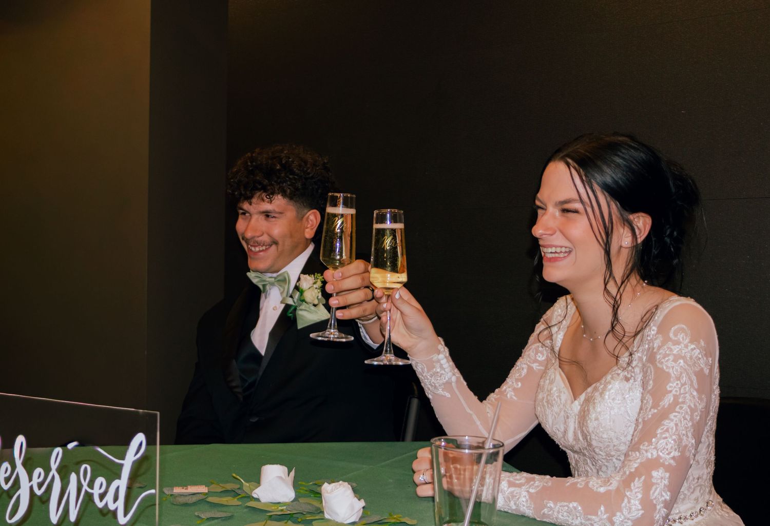 Bride and groom toasting with champagne glasses at wedding reception sweetheart table.