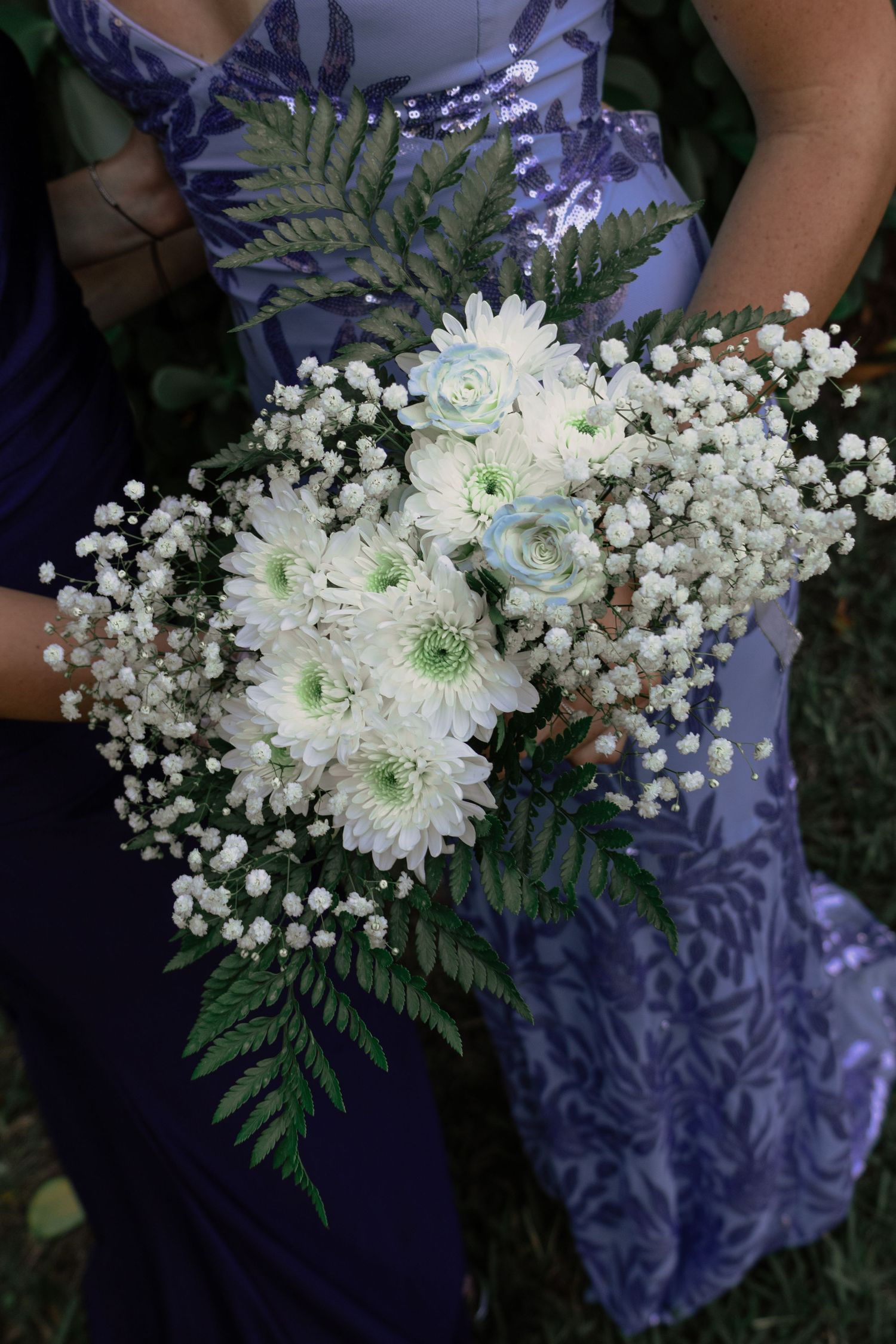 Bridesmaid in lavender dress holds white chrysanthemum and baby's breath bouquet with ferns.