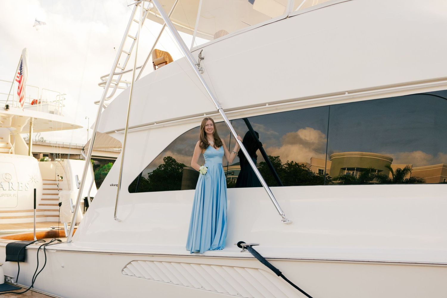 A teenage girl in a light blue satin prom dress stands elegantly on a white yacht deck.