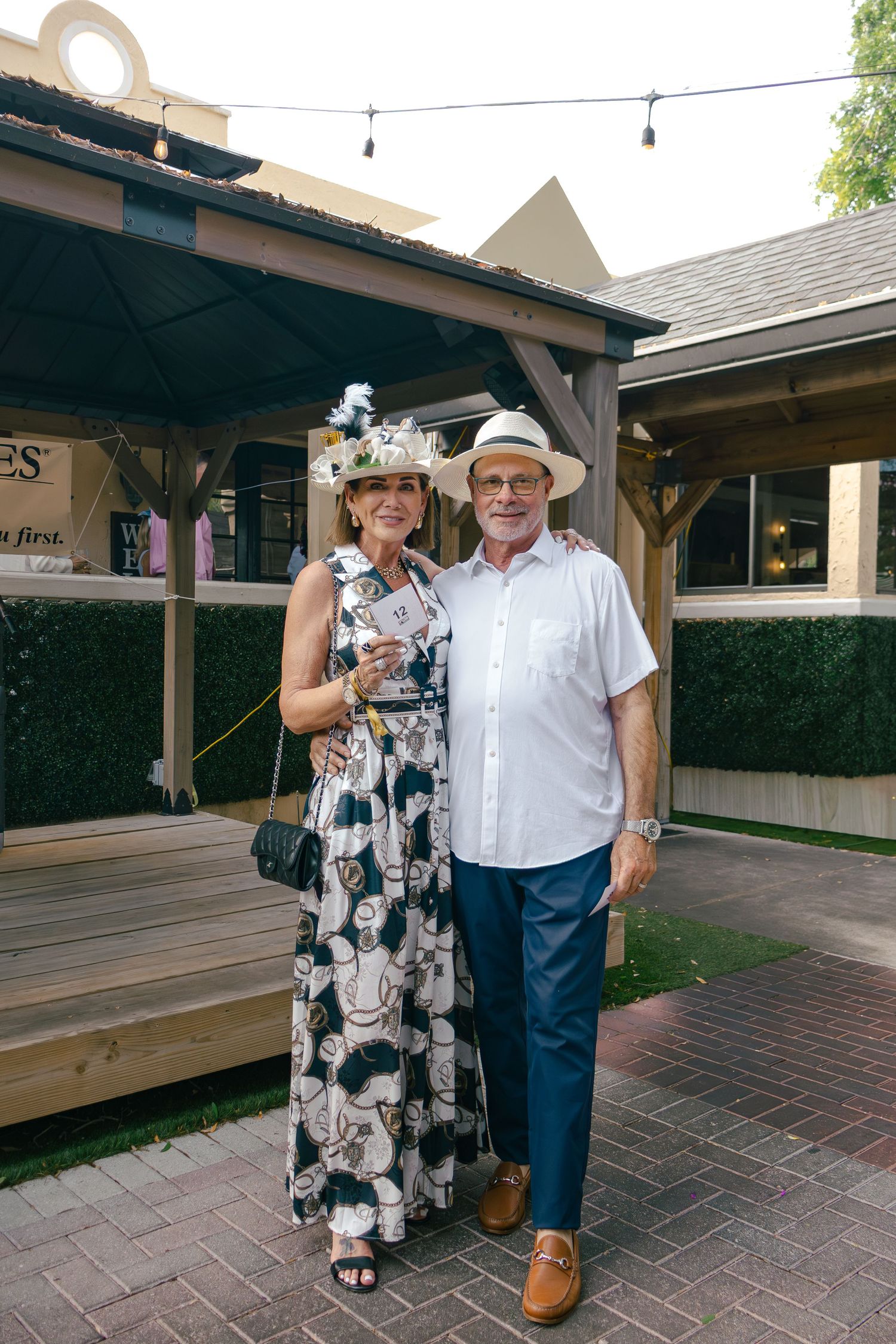 Couple in Kentucky Derby attire posing at outdoor Raymond James financial sponsored event.