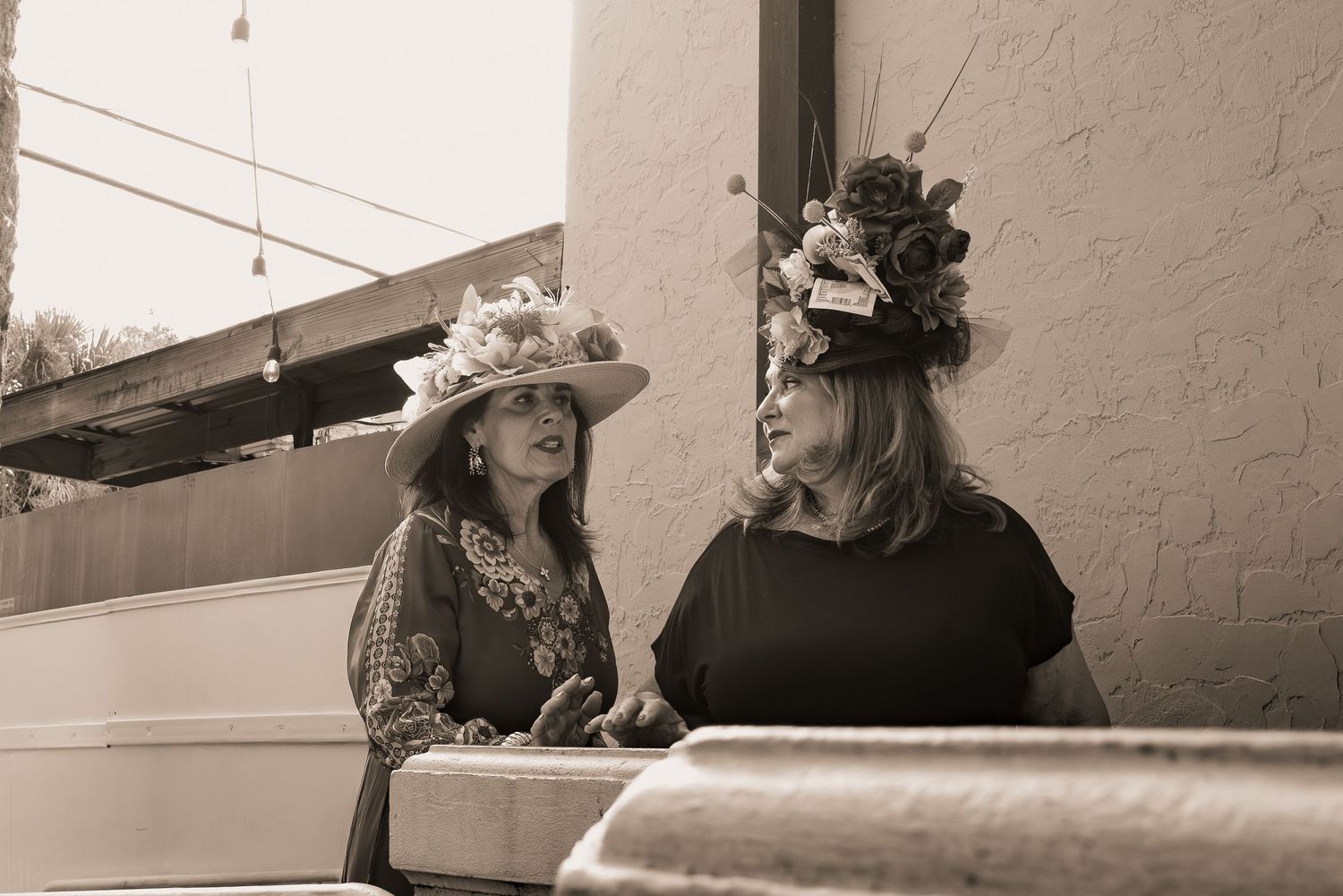 Two women in elaborate decorative hats conversing at a Kentucky Derby themed event.