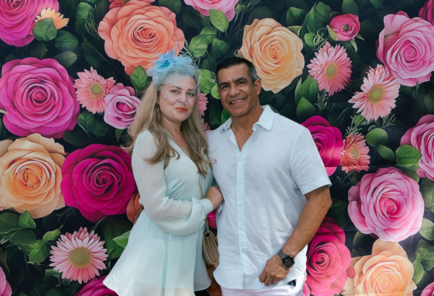 Couple smiling together in front of a vibrant pink and orange floral rose backdrop at a party.