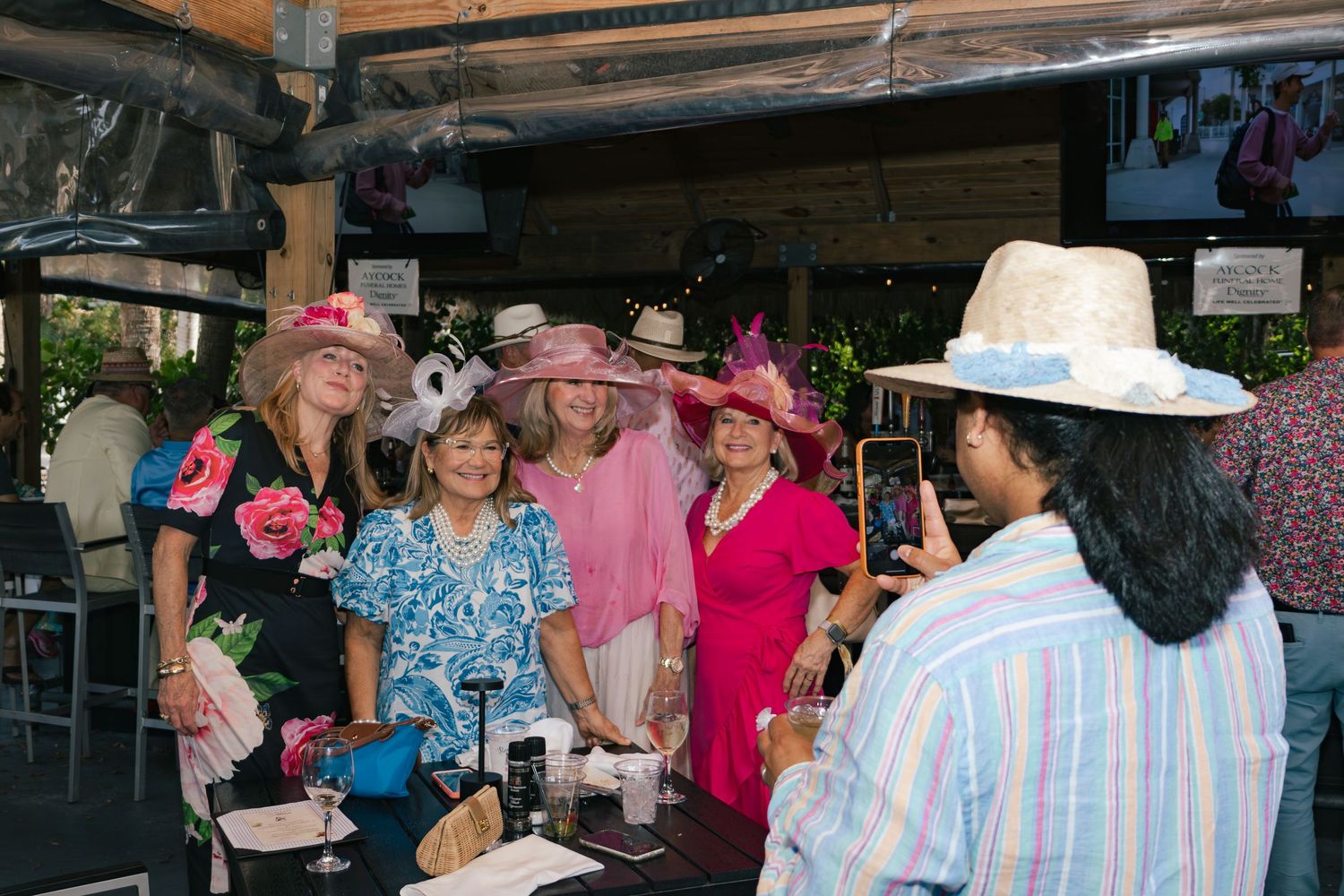 Group of women in colorful Kentucky Derby hats posing for a photo at an outdoor event.