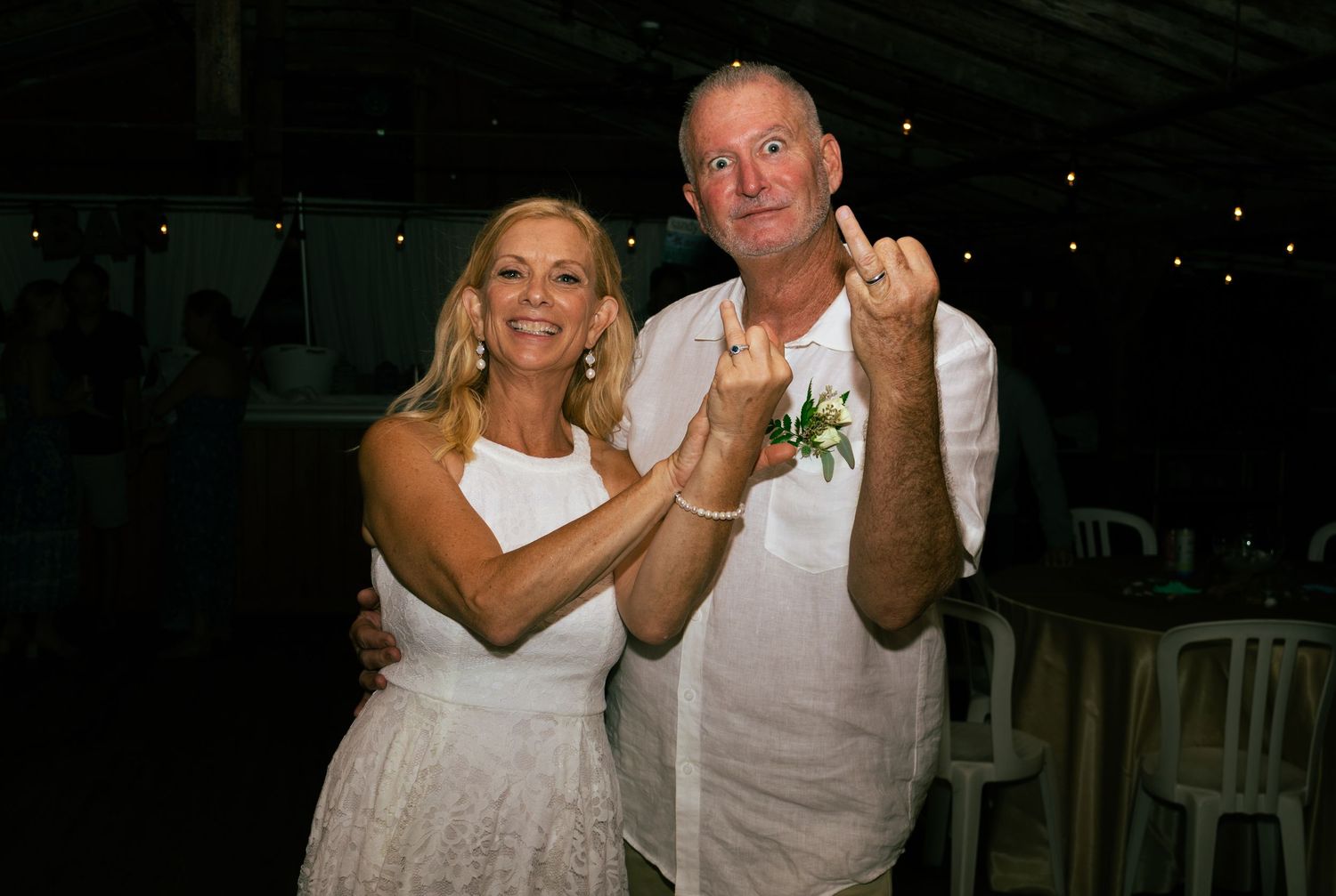 Happy newlywed couple posing together at their wedding reception, groom showing off wedding ring with a smile.