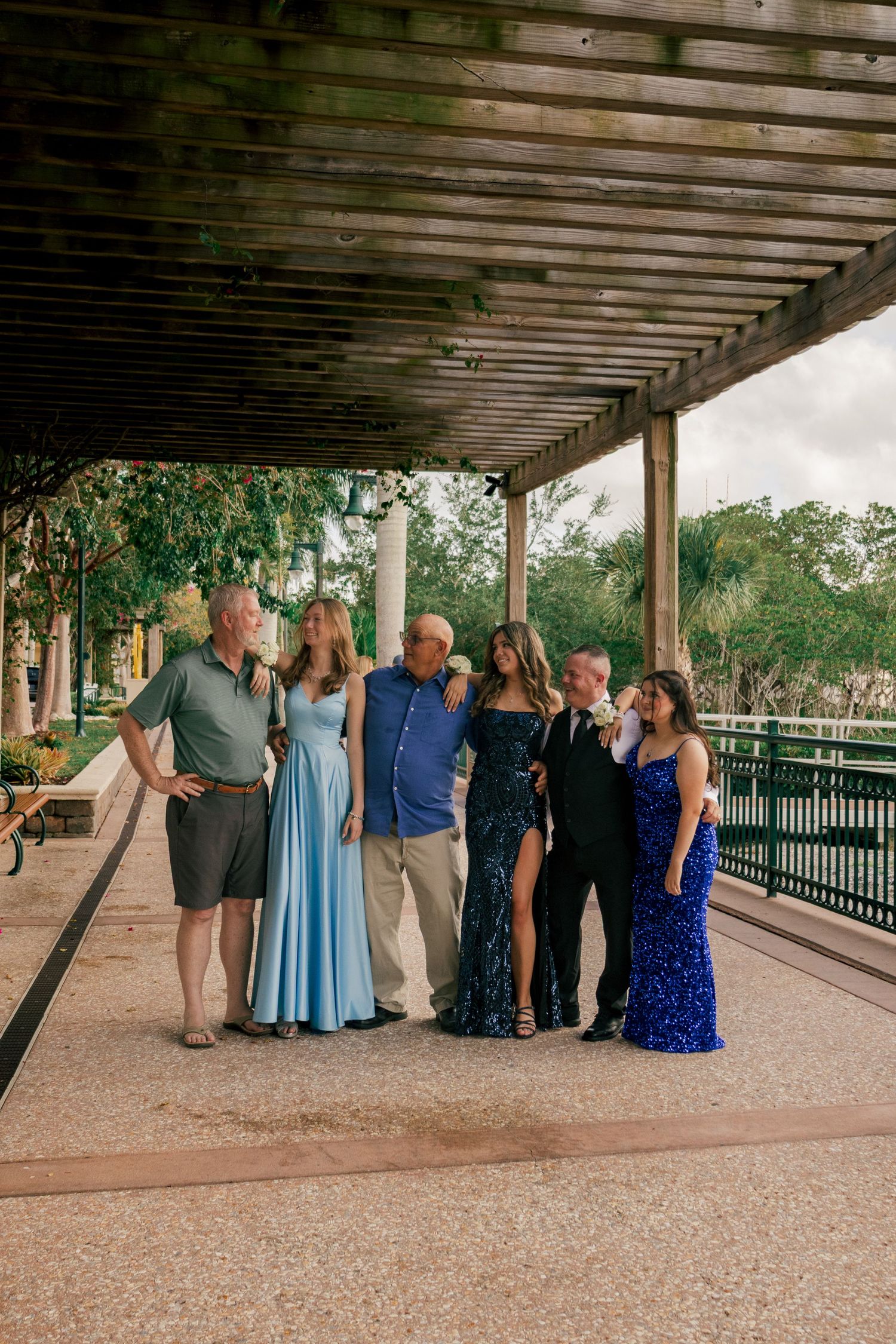 Family photo with teens in prom dresses and adults gathered under a rustic wooden pergola.