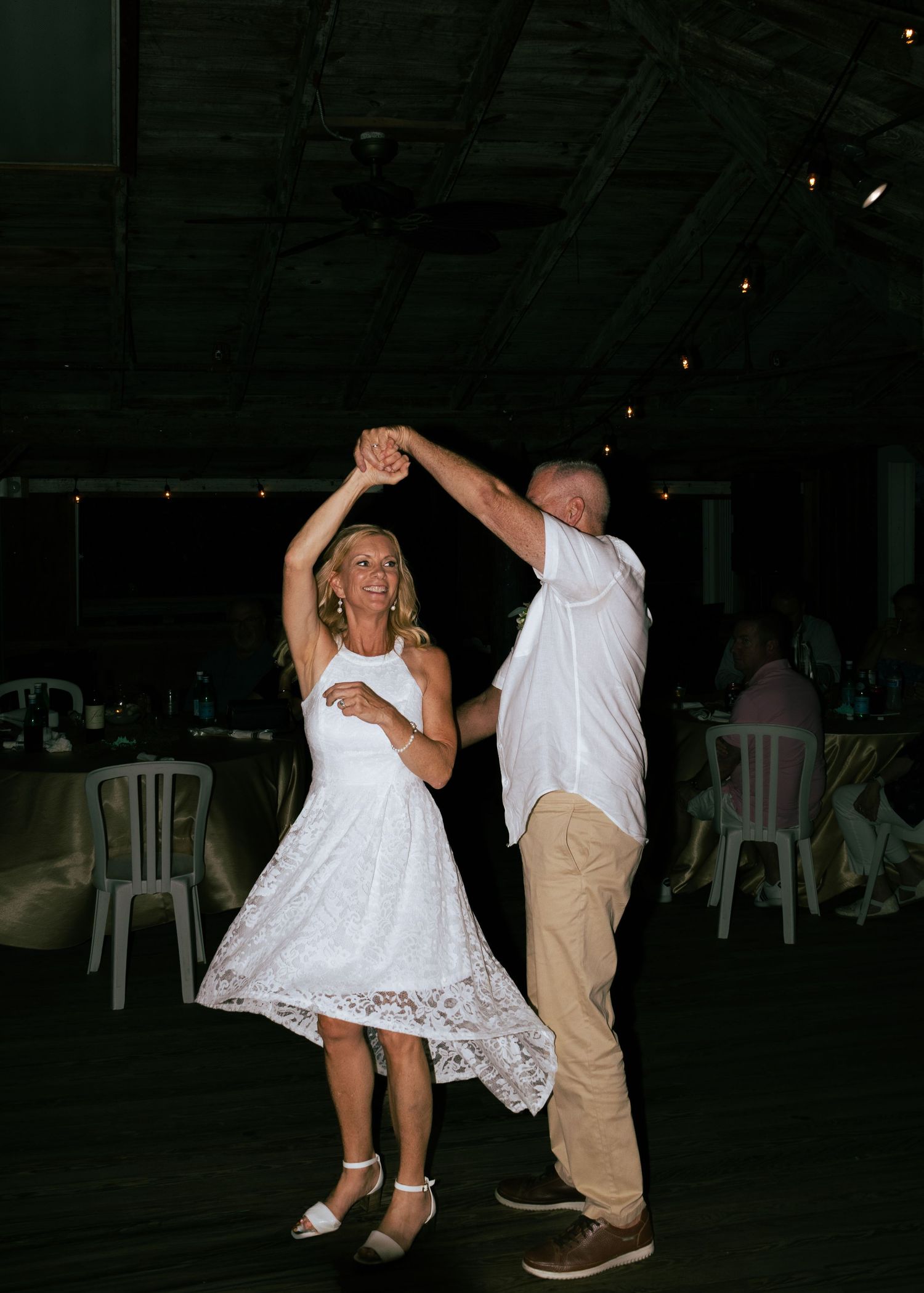 Bride and groom dancing joyfully during evening wedding reception in dimly lit venue.