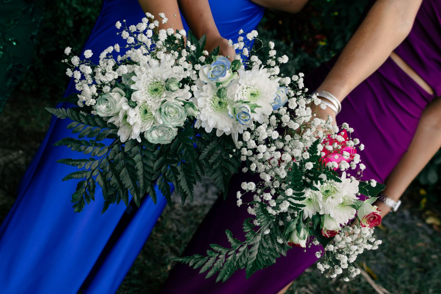 Bridesmaids holding elegant bouquets of white roses, succulents, and baby's breath in blue and purple gowns.