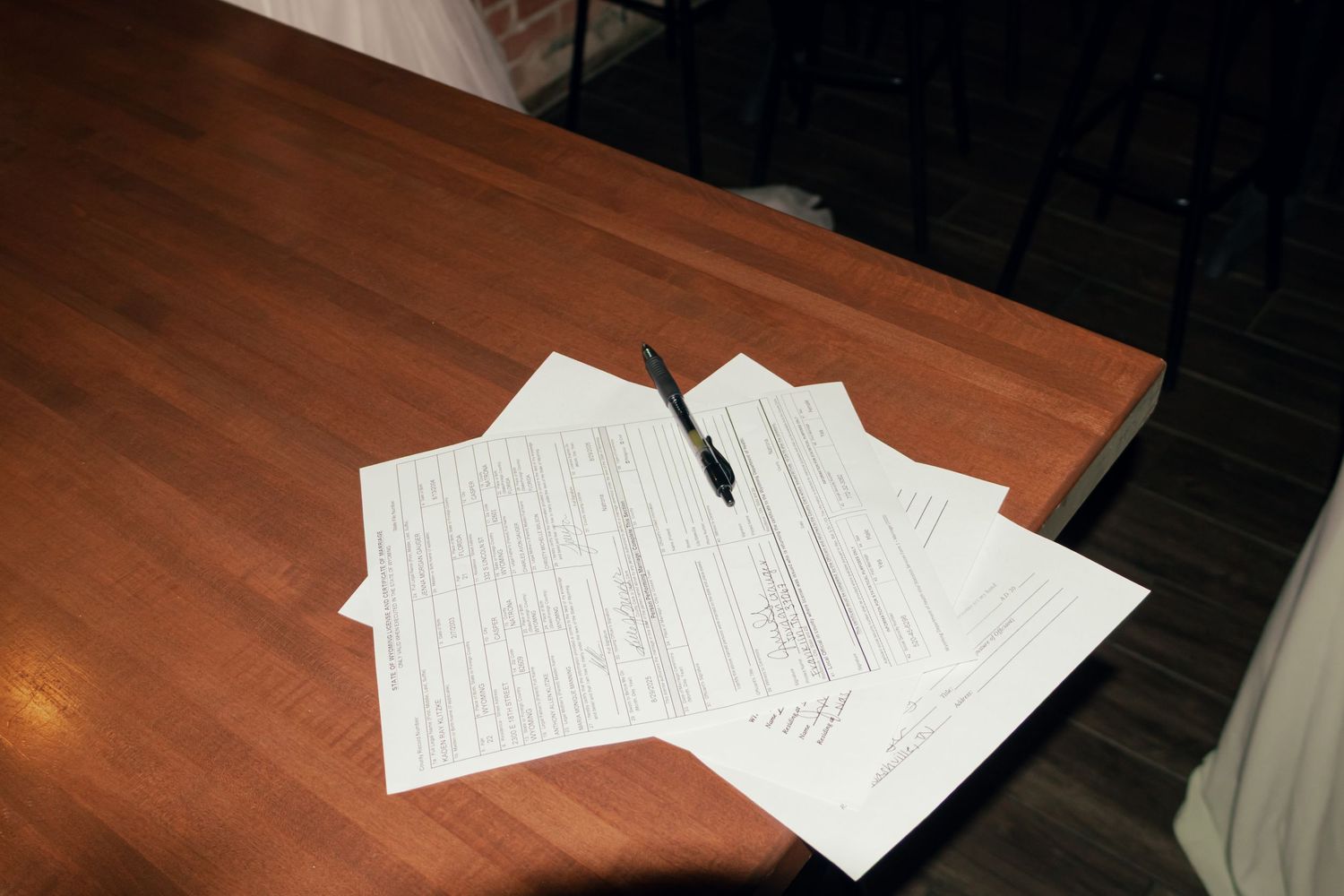 Wedding documents and pen on wooden table at rustic venue.