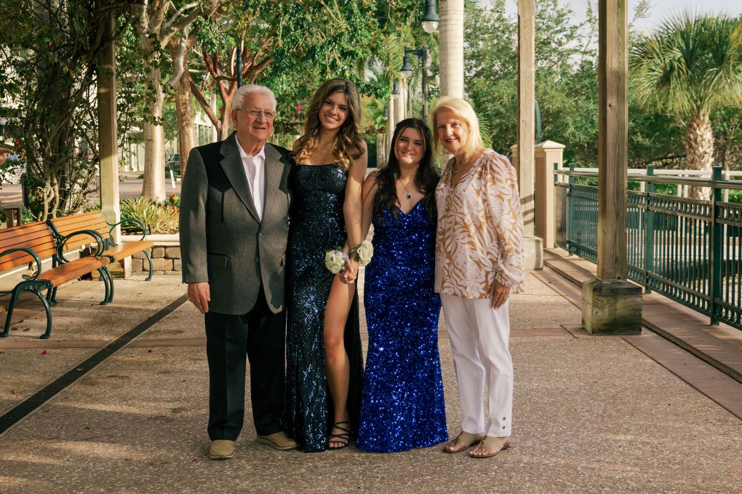 Group of four people posing together under a pergola with two young women in formal gowns.