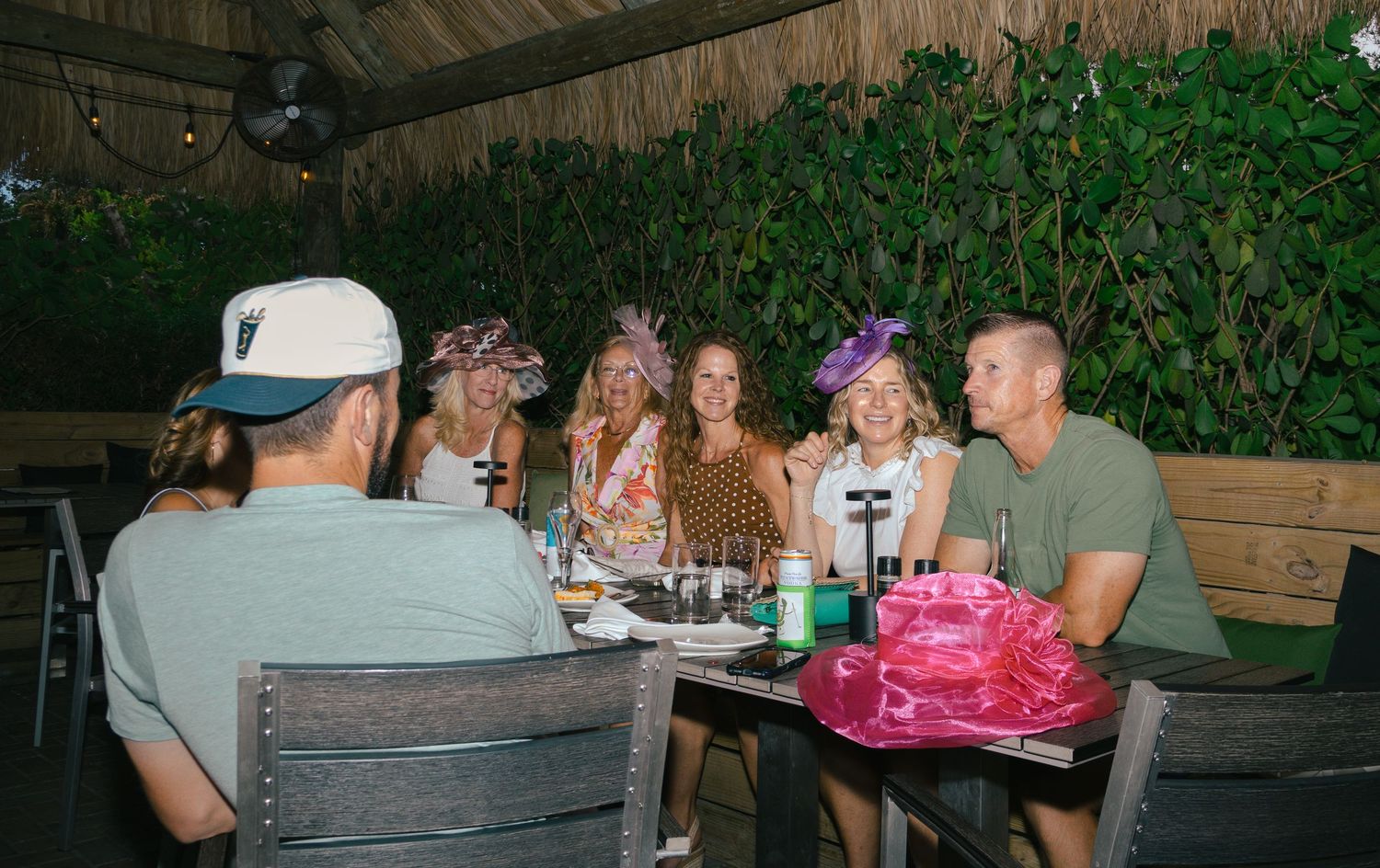 Group of friends wearing festive hats dine together at outdoor restaurant table.
