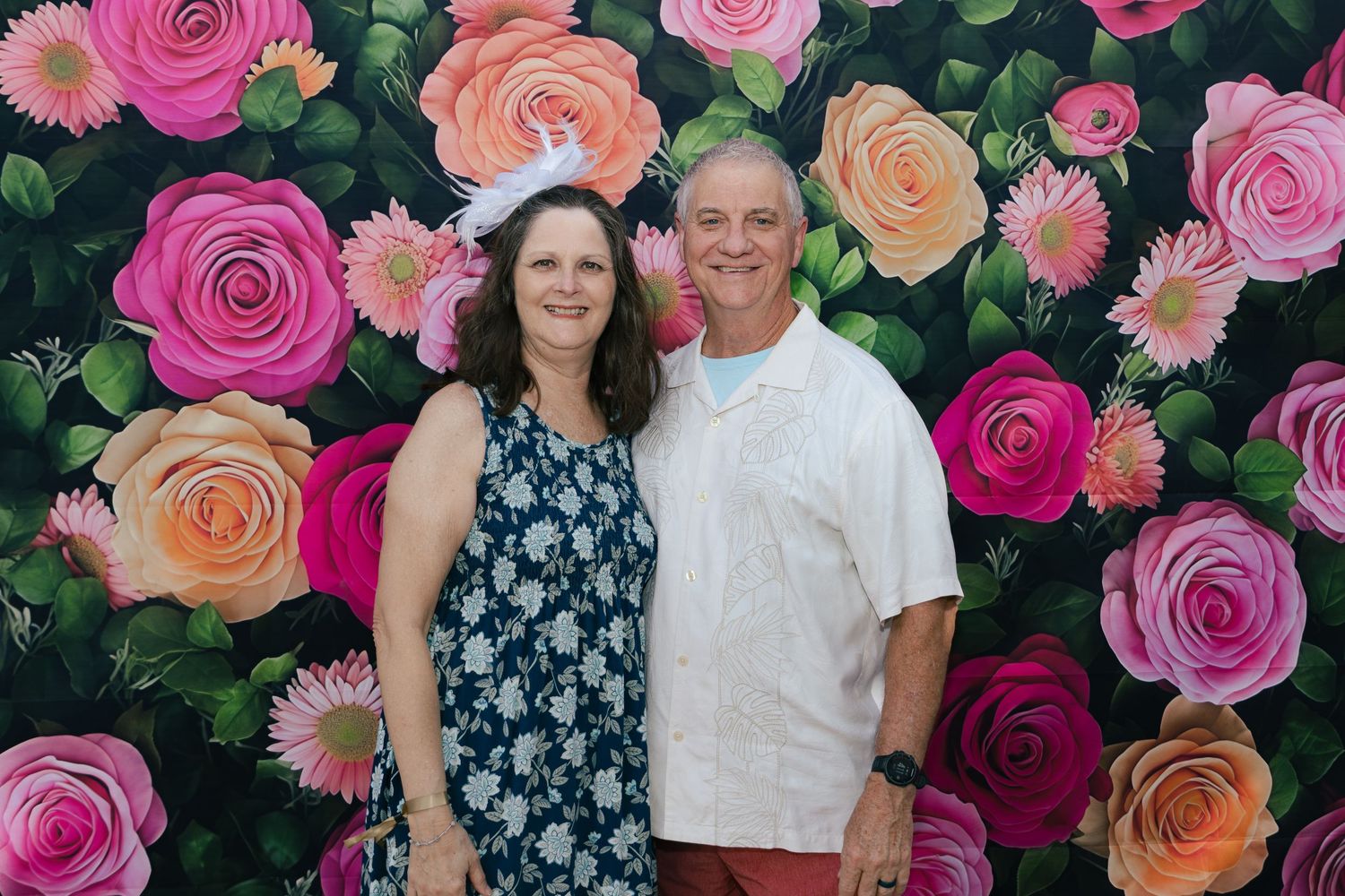 Smiling couple posing together in front of a colorful painted floral rose backdrop at an outdoor event.